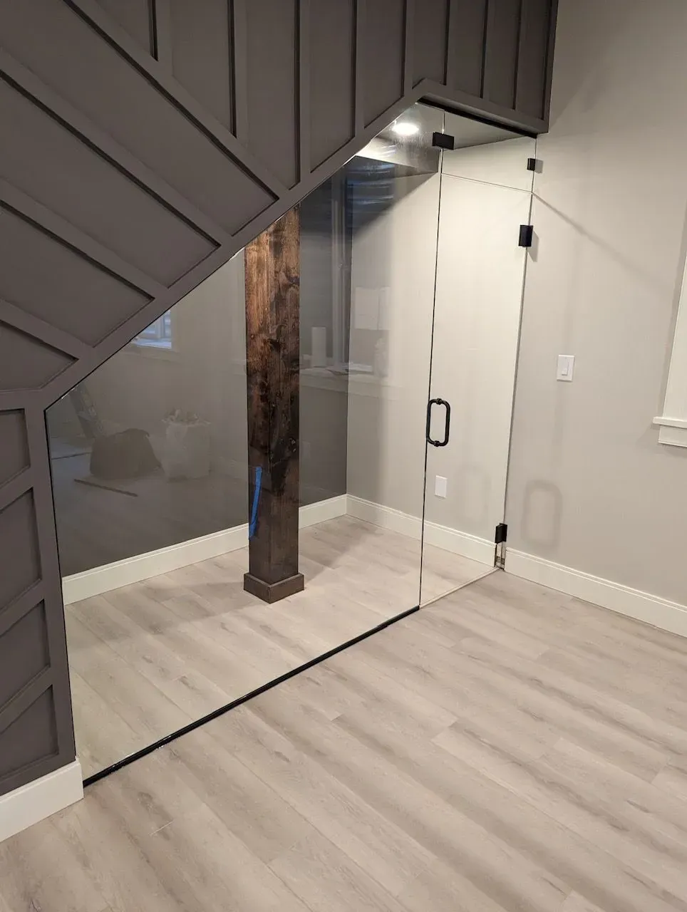 Modern staircase beside a glass railing and wood support post in a bright hallway