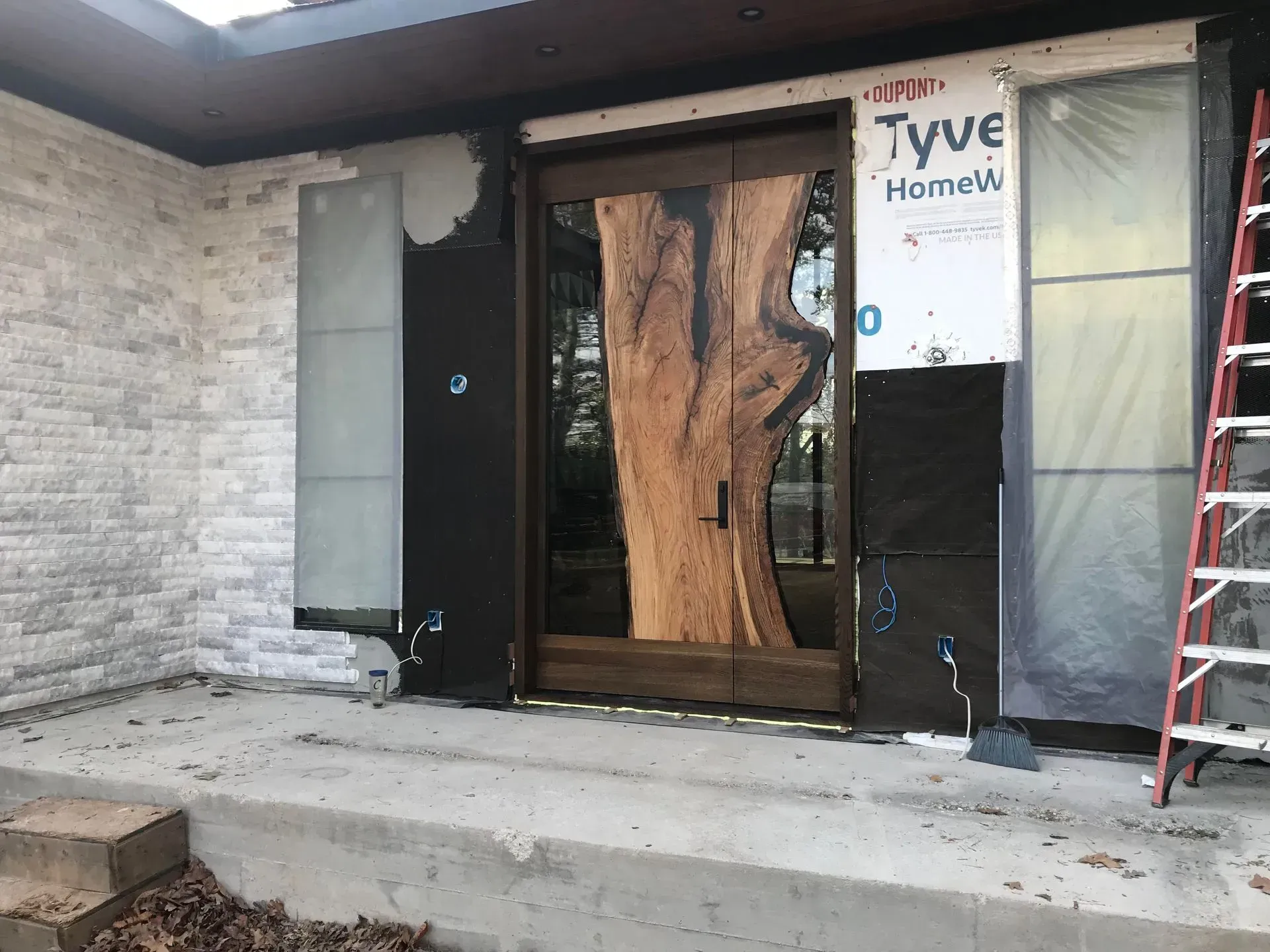 Partially finished house entry with black trim, wood door, and a red ladder beside the porch