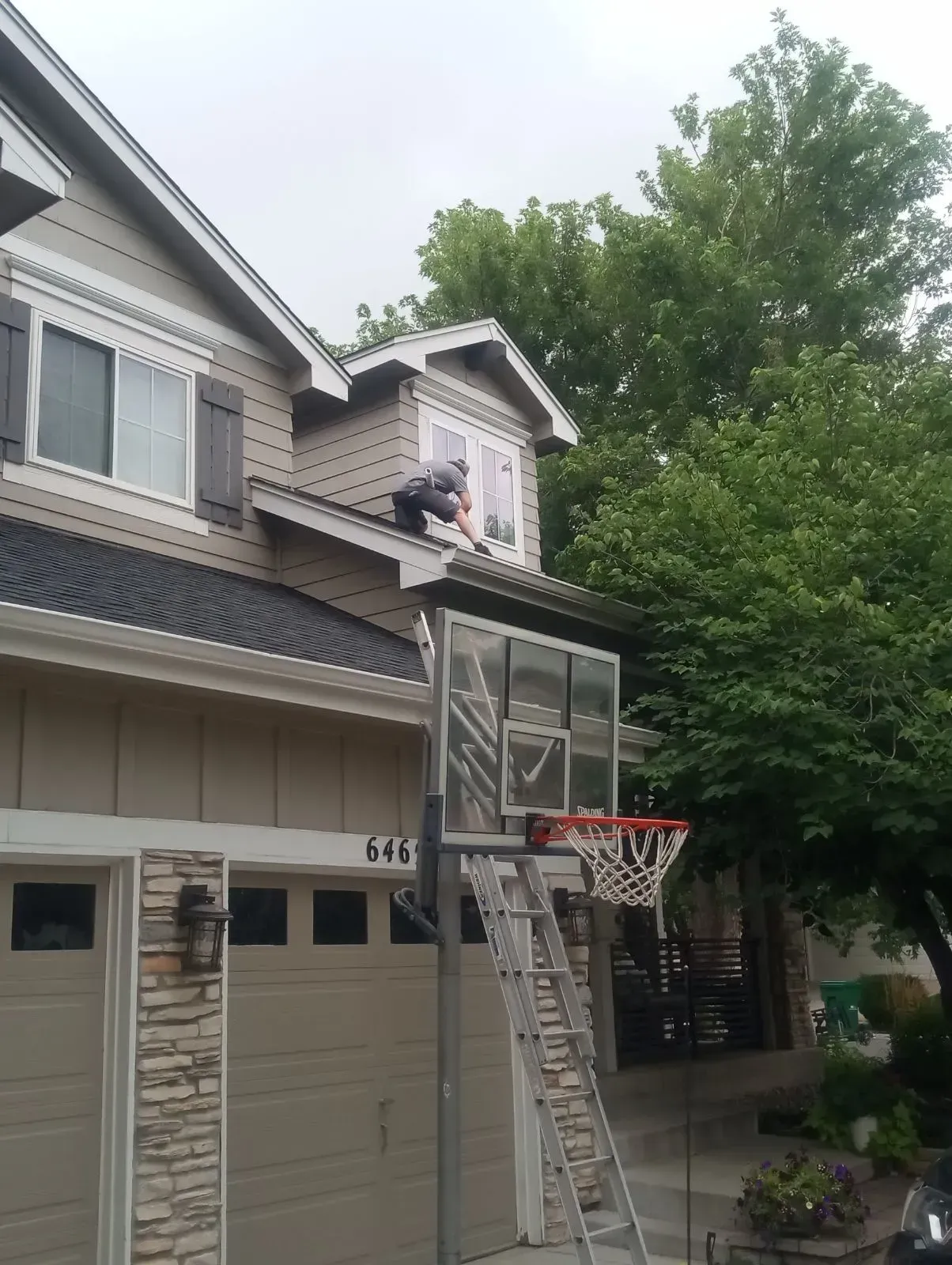 Suburban garage with a basketball hoop and a person on the second-floor window ledge