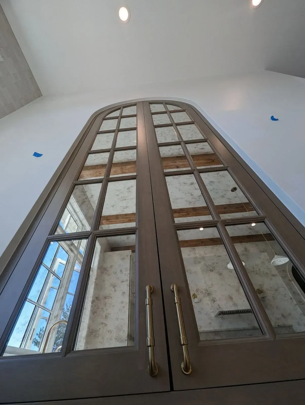 Tall arched wooden double doors with glass panes in a white room, viewed from below.
