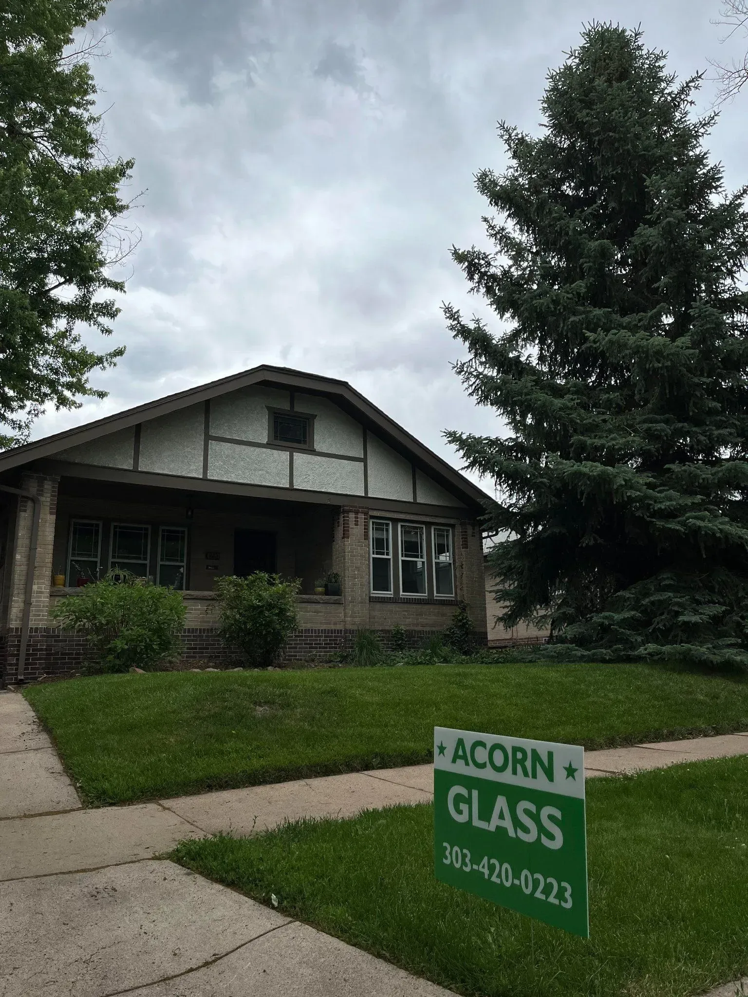 House with lawn and trees; green sign reads “ACORN GLASS” in the front yard.