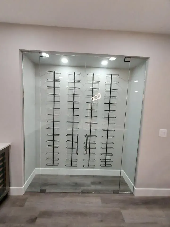 Glass-walled wine display room with empty metal racks and overhead lights in a modern interior.