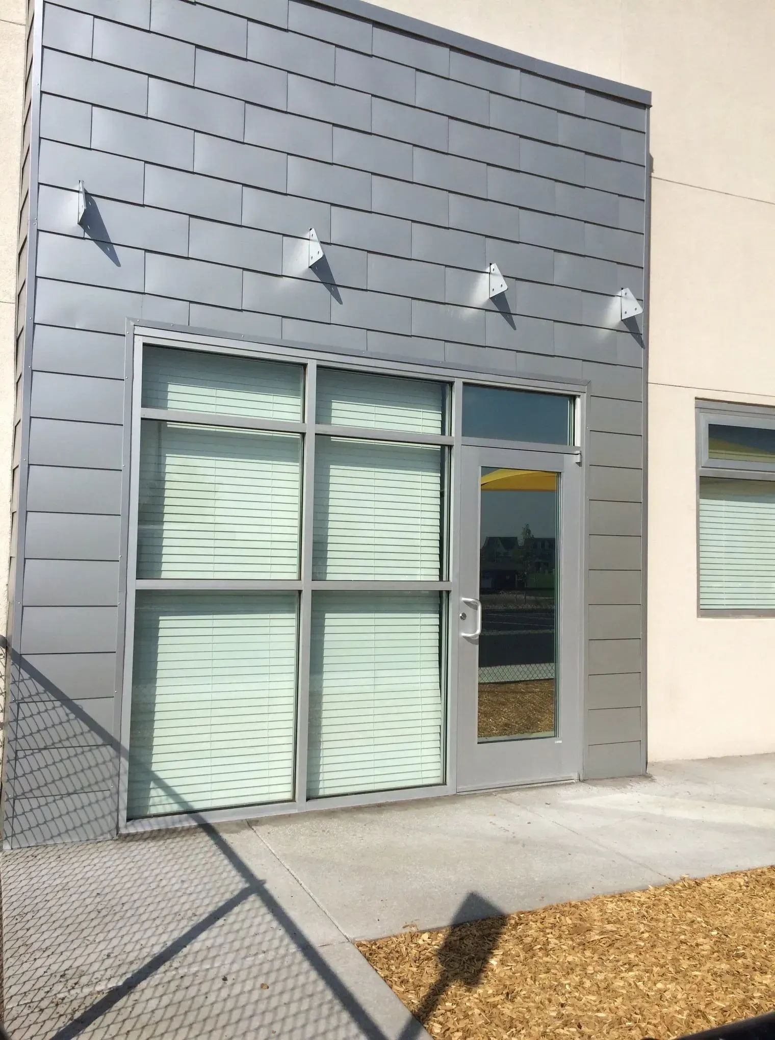 Modern building entrance with gray siding, glass doors, and exterior wall lights