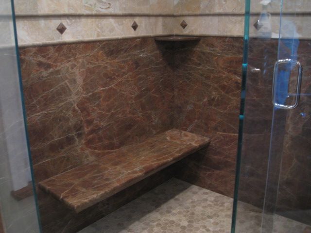 Brown marble shower stall with bench inside.