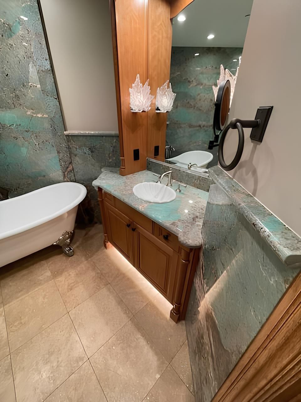 Luxury bathroom with marble walls, double vanity, large mirror, soaking tub, and beige tile floor