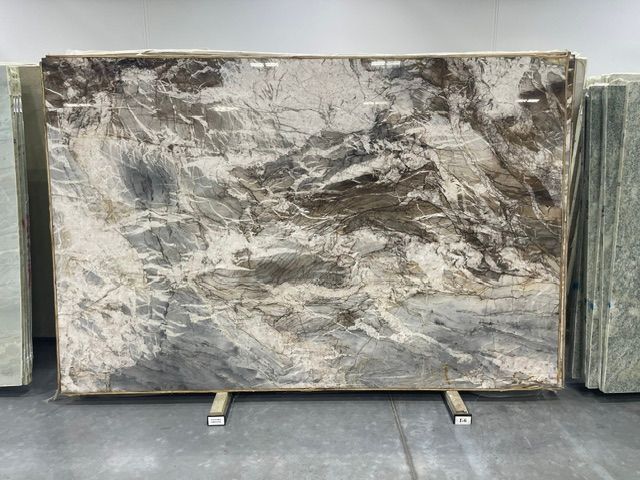 Large gray-and-white marble slab displayed on metal supports in a stone yard.