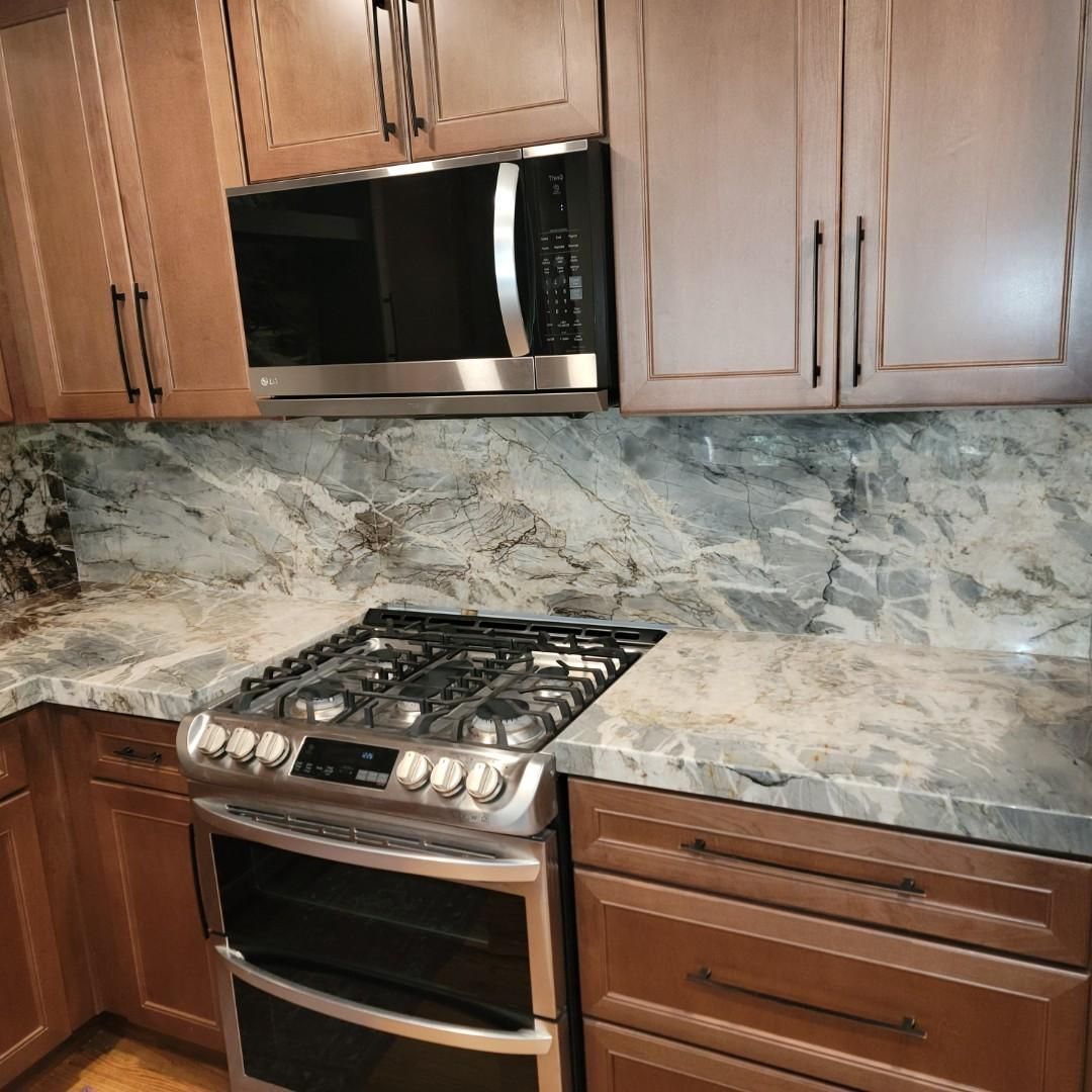 Modern kitchen with wooden cabinets, stainless steel stove and microwave, and marble backsplash.