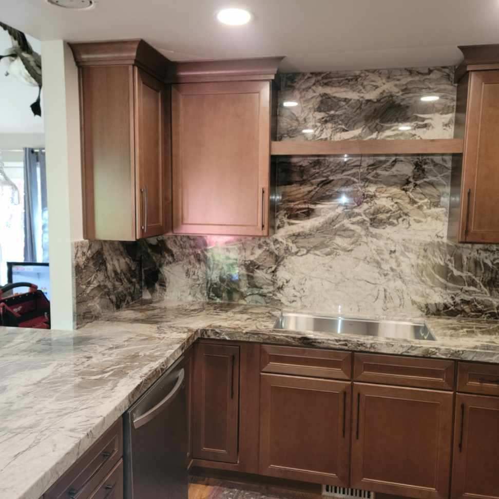 Modern kitchen with dark wood cabinets, marble-look backsplash, and stainless steel sink.