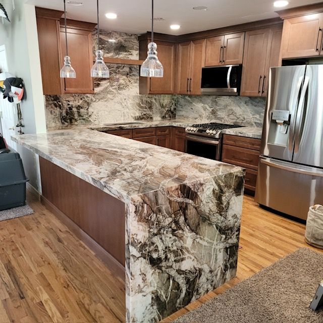 Modern kitchen with a marble island, wood cabinets, stainless appliances, and pendant lights.