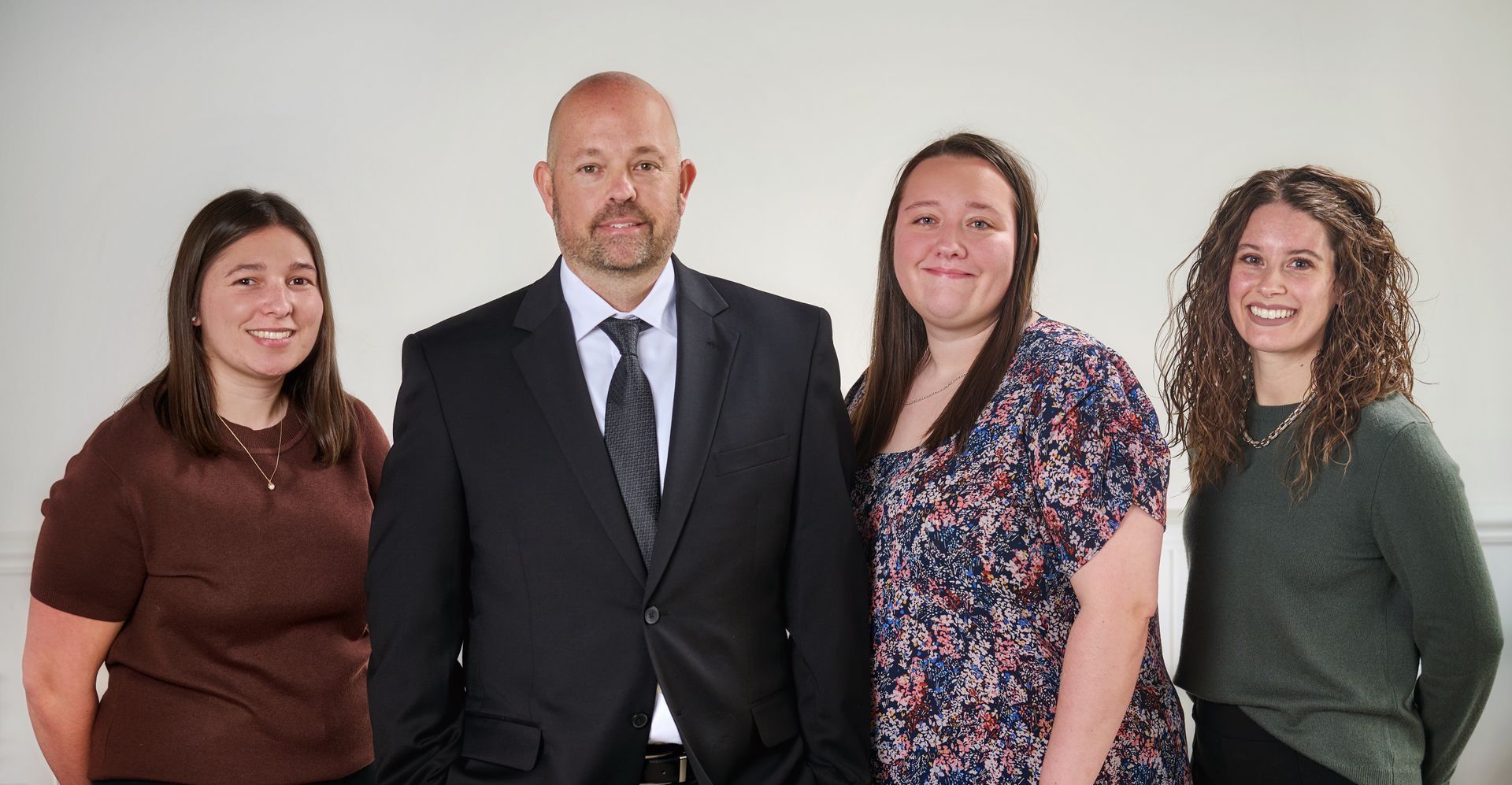 Four people standing side by side against a white background, dressed in formal and casual attire.