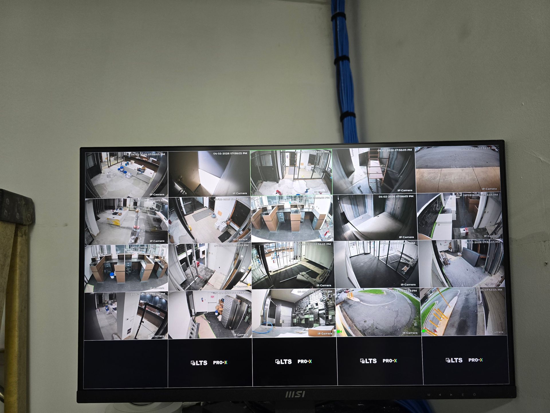 Wall-mounted CCTV monitor showing a 4x4 grid of security camera views in a room.