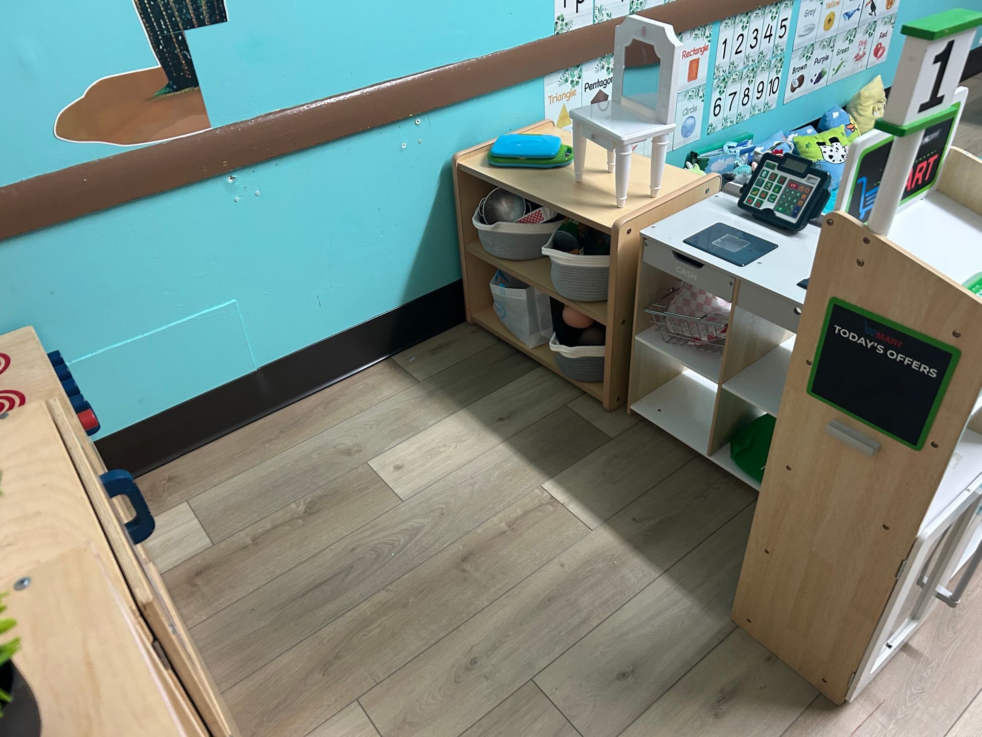A preschool classroom corner with shelves, a small desk, and a tiny white chair.
