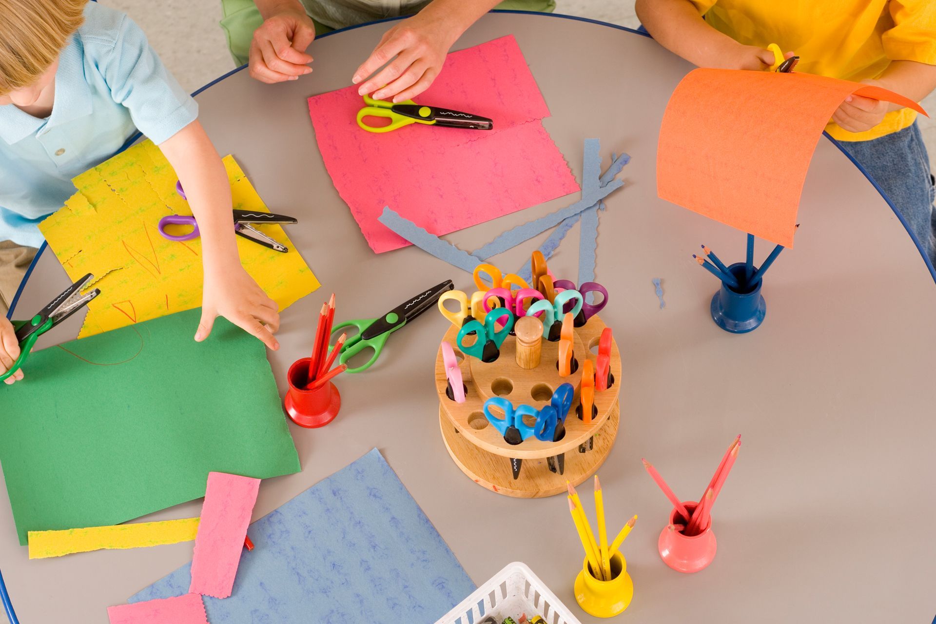 A group of children are sitting at a table cutting paper with scissors