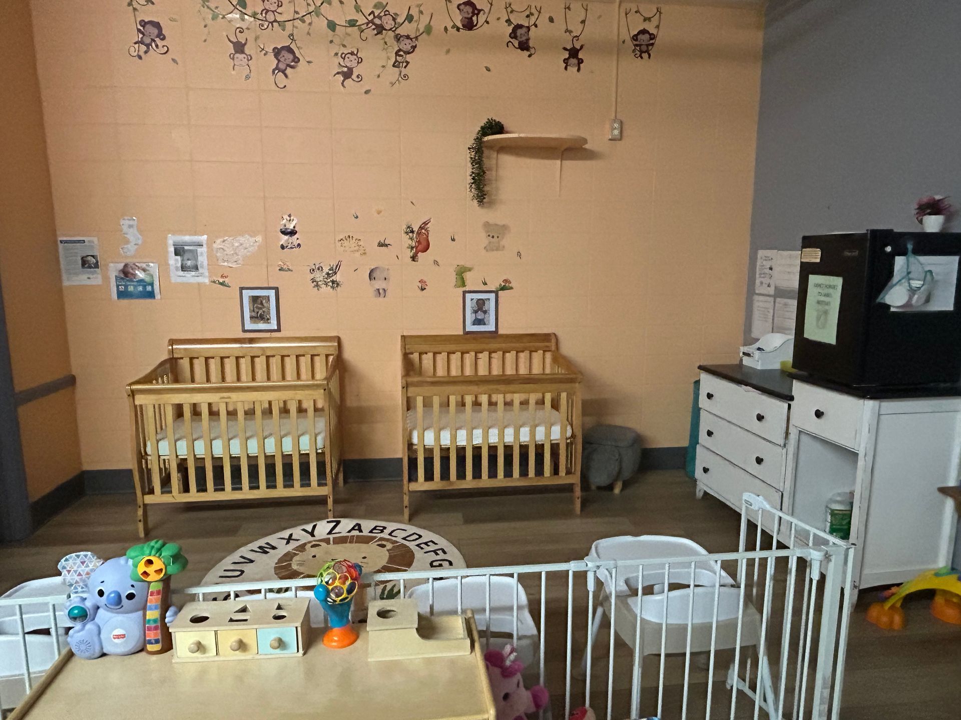 Nursery room with two cribs, a changing table, and a small play area. Light orange walls.