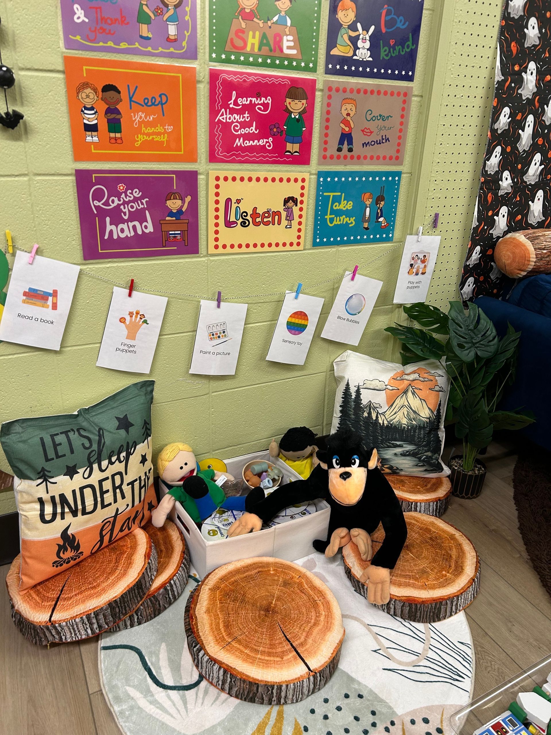 Classroom corner: posters, drawings, pillows on log stools, and stuffed toys.