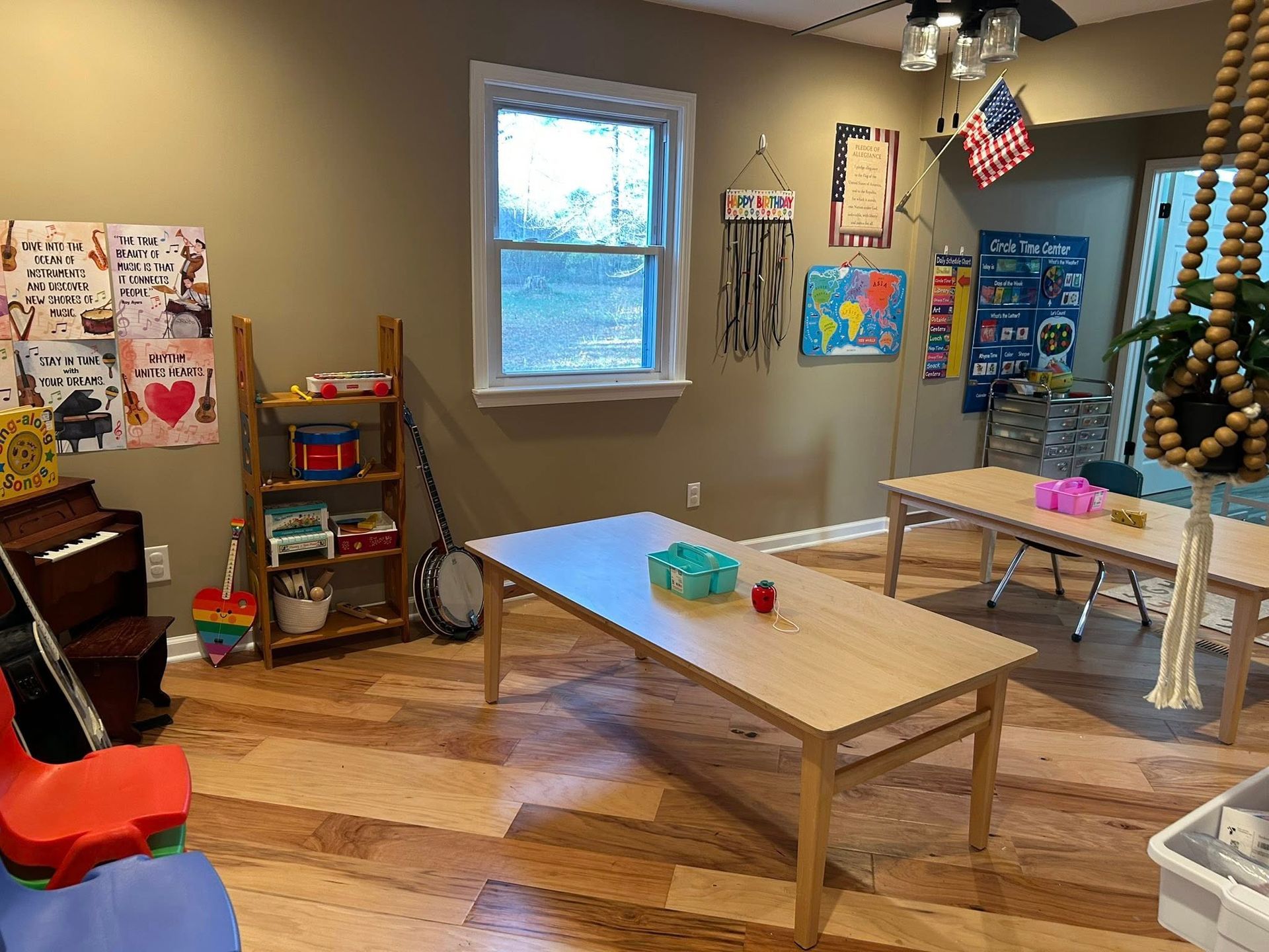 Playroom with wooden floor, two tables, shelves with toys, window, and decorations.