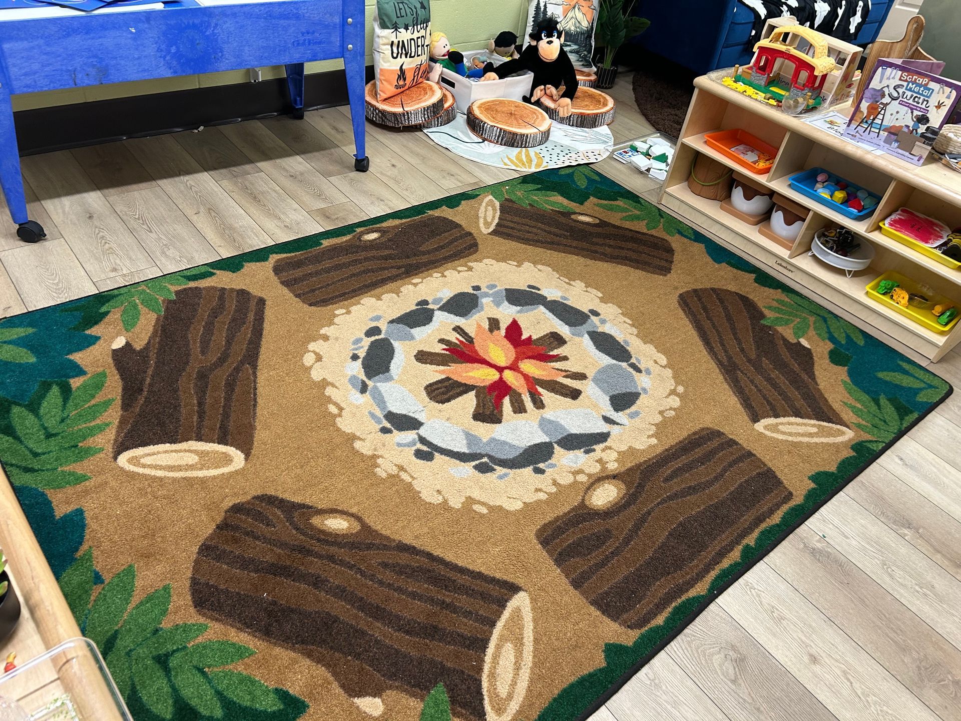 Campfire-themed rug with logs and a fire pit in a room with child-sized furniture and toys.