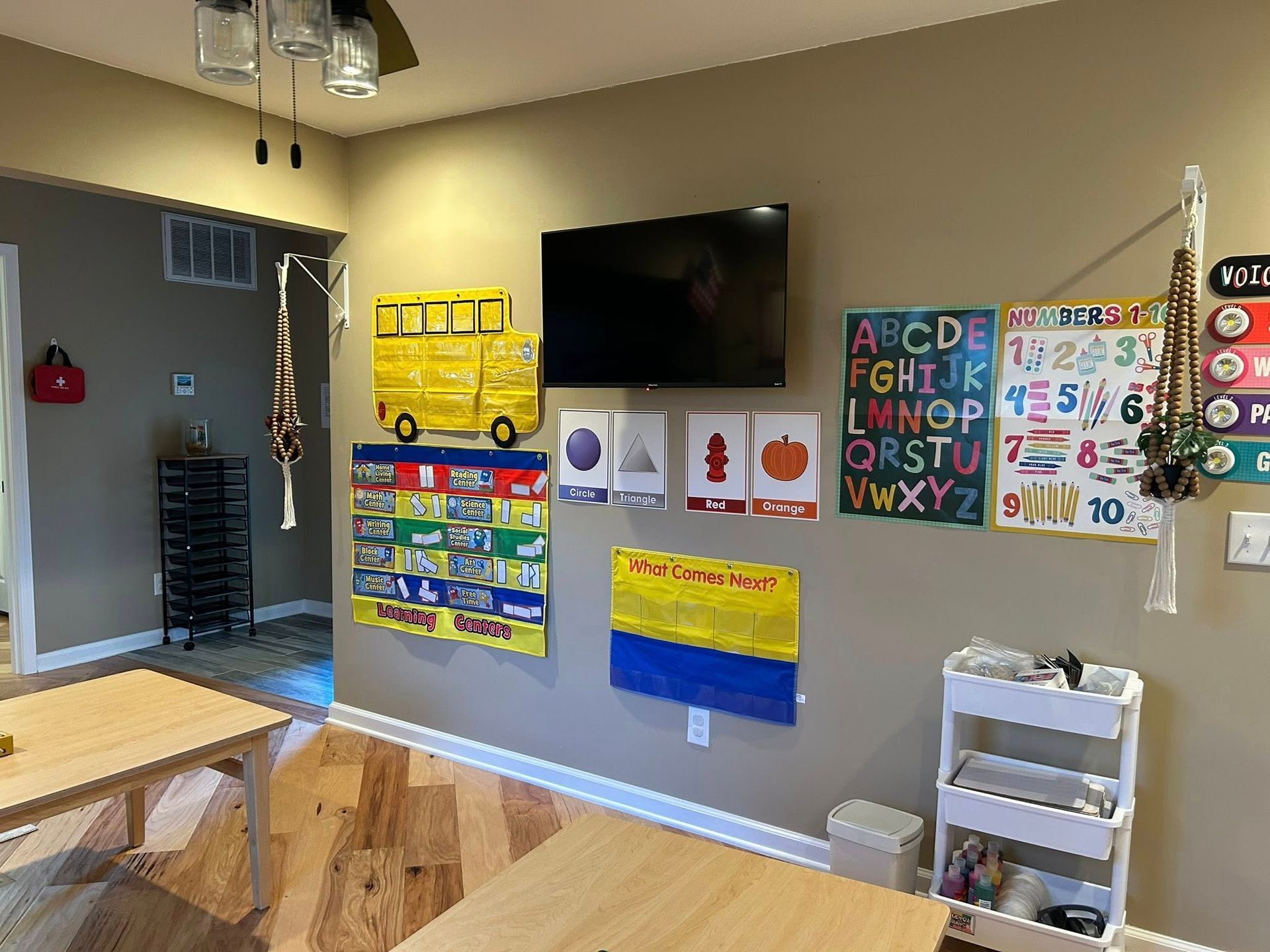 Classroom wall with TV, educational posters, a yellow school bus, and a rolling cart.