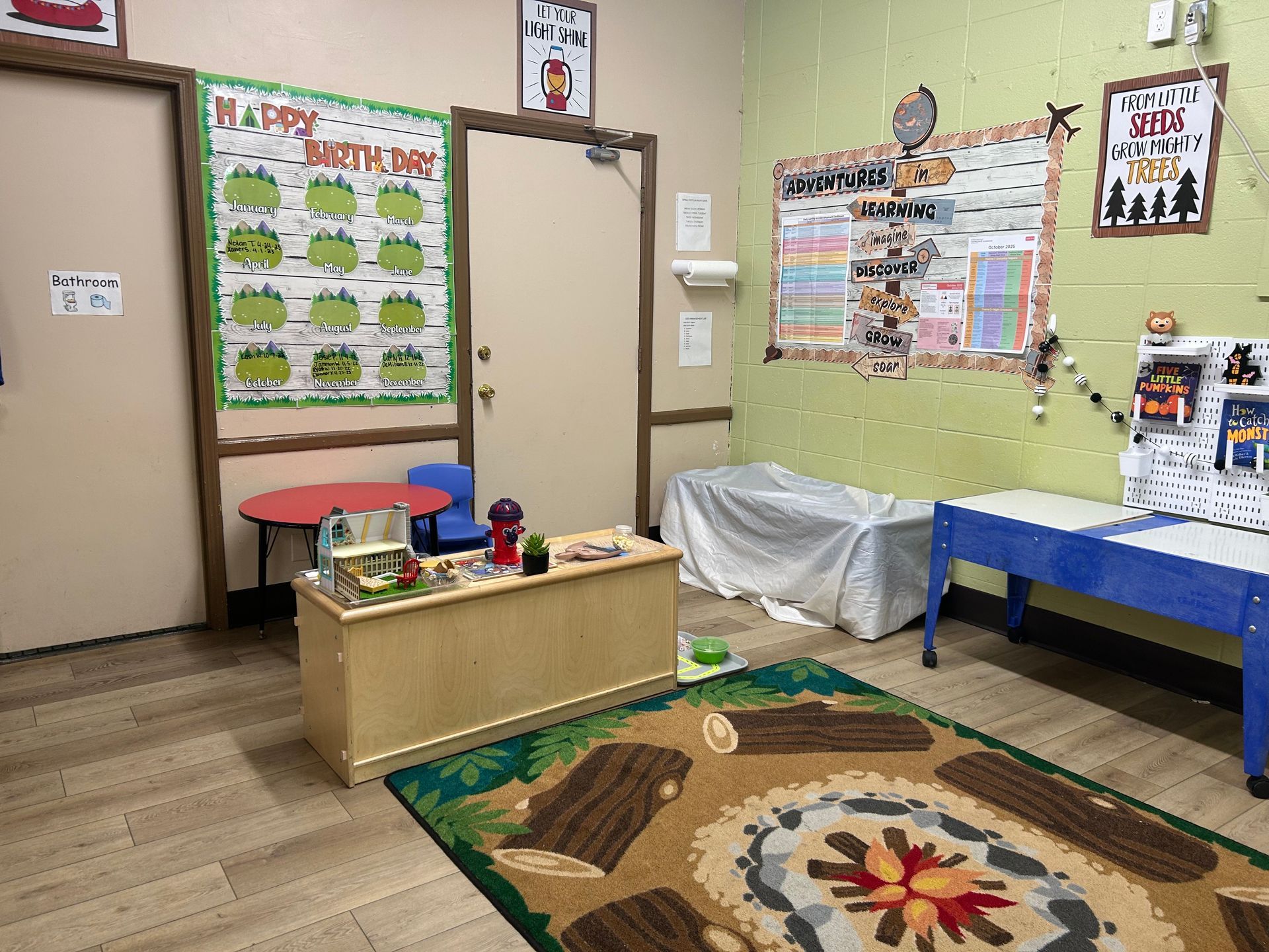 A brightly lit classroom with tables, a rug, and educational posters.