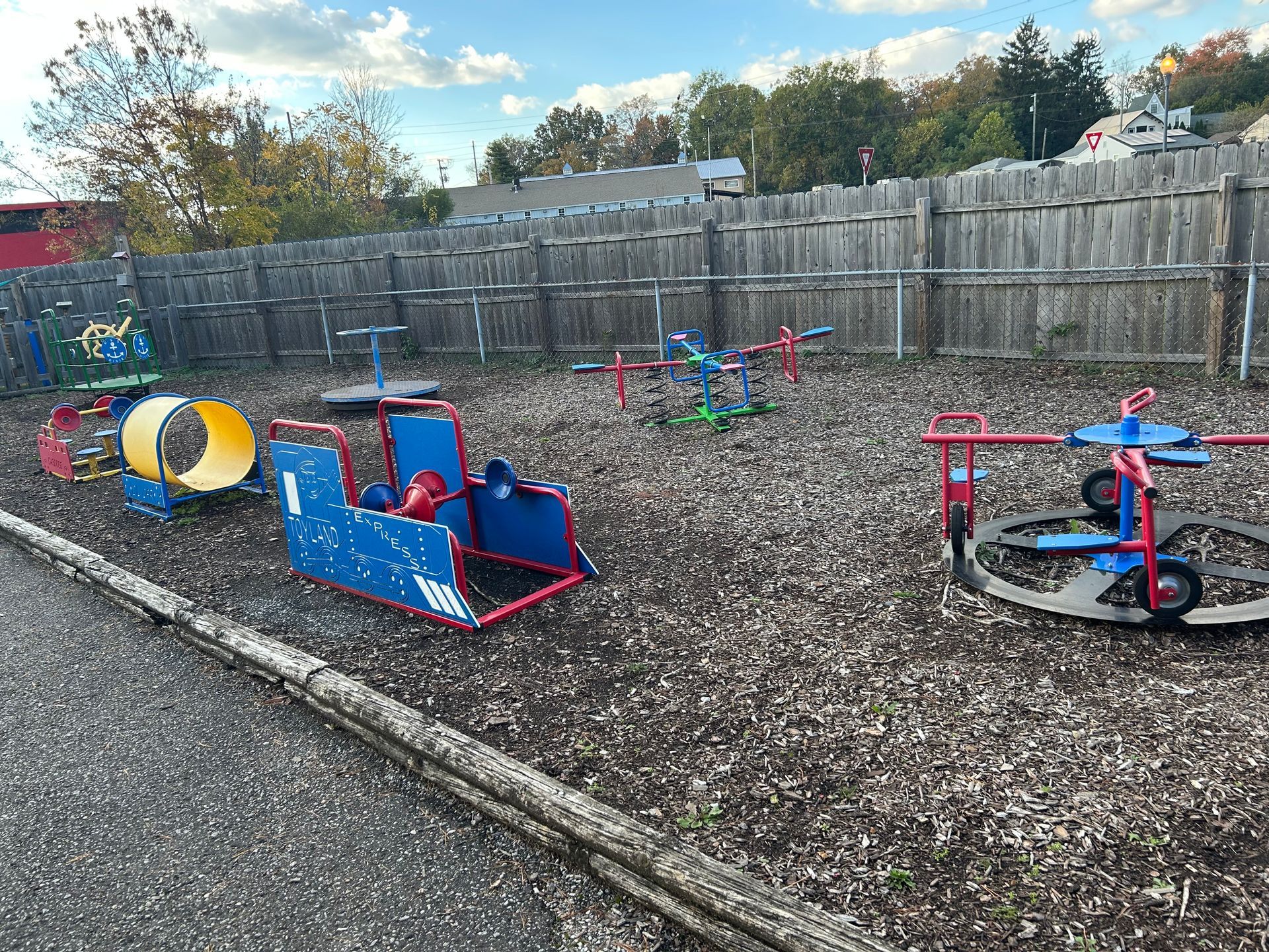 Playground with blue and red equipment, wood chip ground, and wooden fence.
