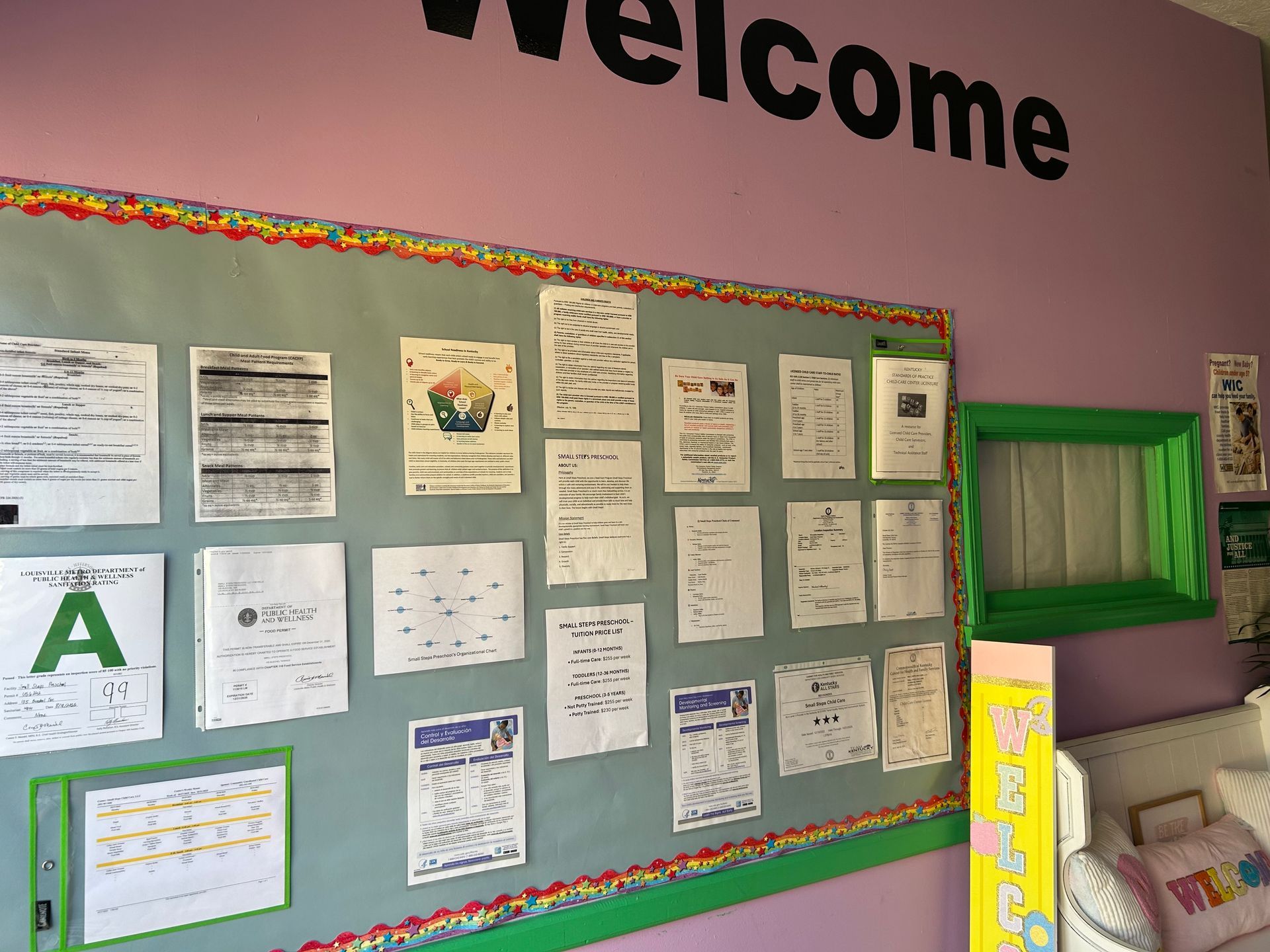 Bulletin board with documents on a pink wall. Green border and welcome sign.