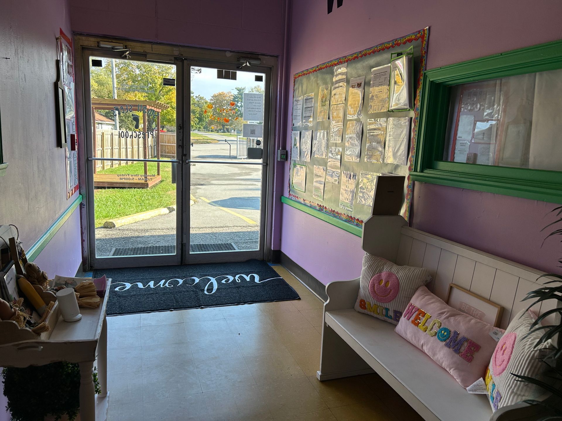 Entryway with purple walls, white bench, open doors, and welcome mat.