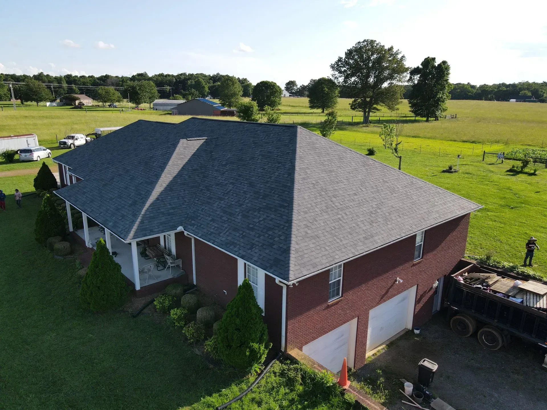 Aerial view of a brick house with a new gray roof, two-car garage, and lush green yard.
