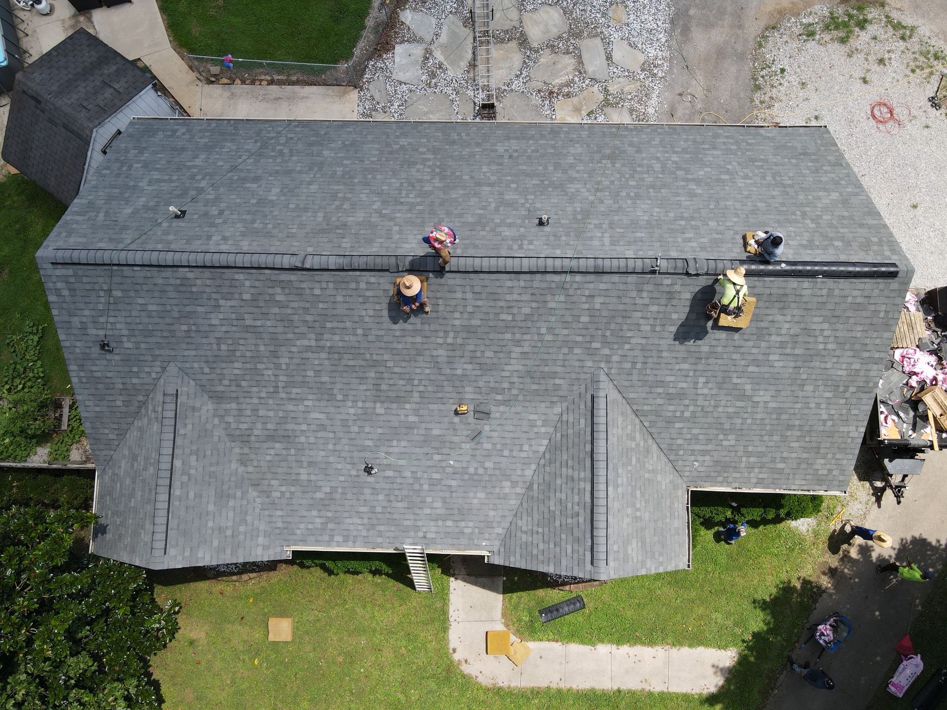 An aerial view of roofers installing gray shingles on a residential home during a sunny day.