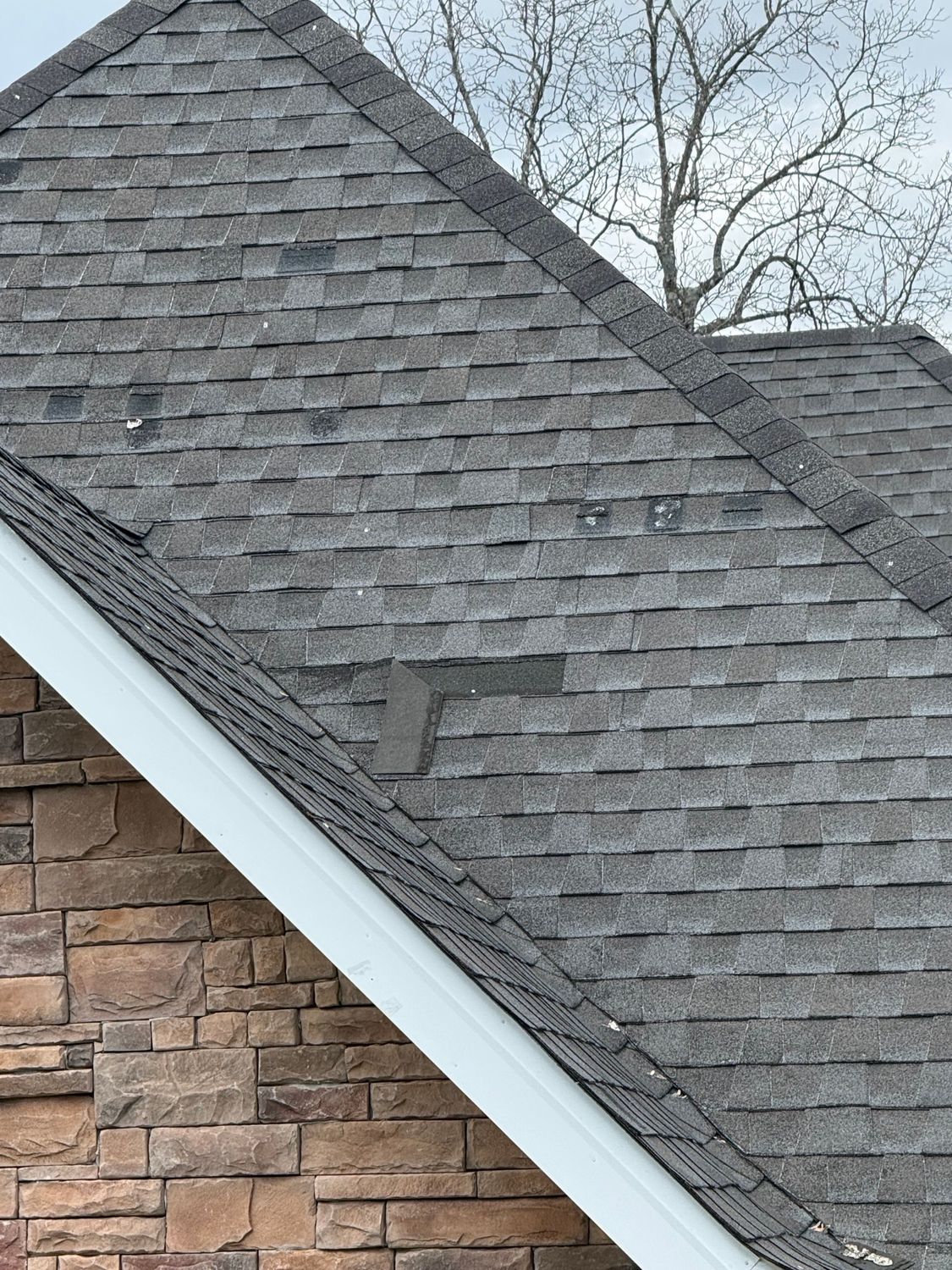 A close-up view of a shingled roof with a single darker, mismatched shingle patch near the edge of the gable.