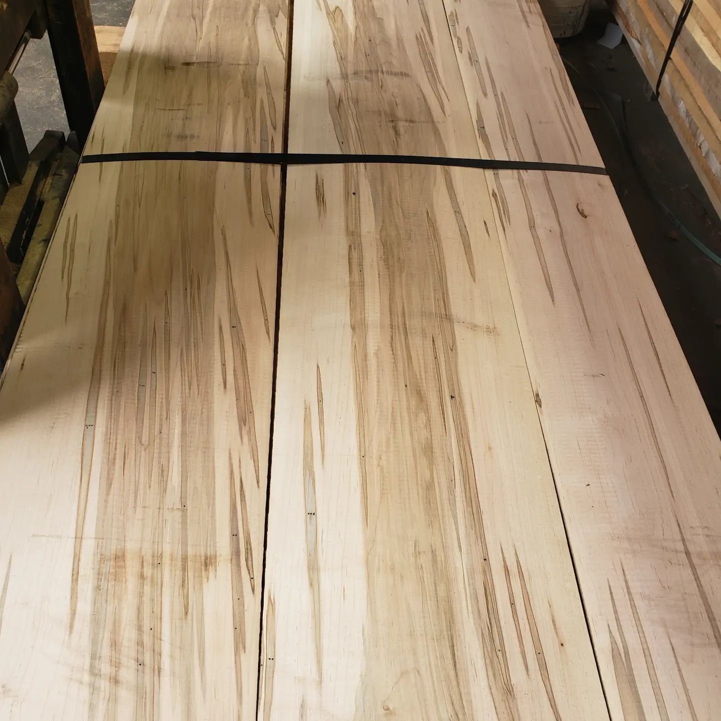 Stacked wooden boards with distinct vertical brown streaks and grain patterns in a warehouse setting.