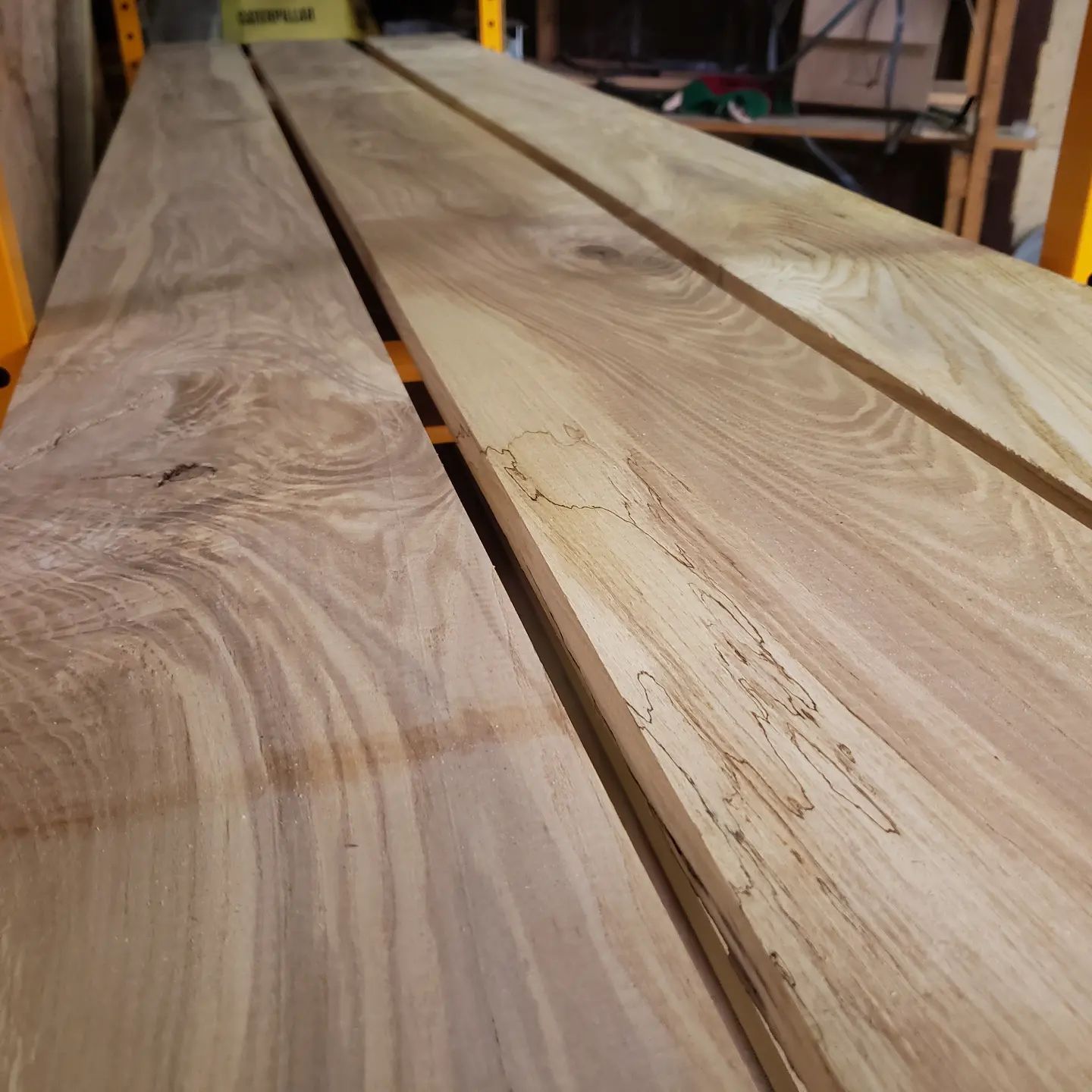 Three long, light-colored wooden planks arranged side-by-side on a yellow workshop shelf.