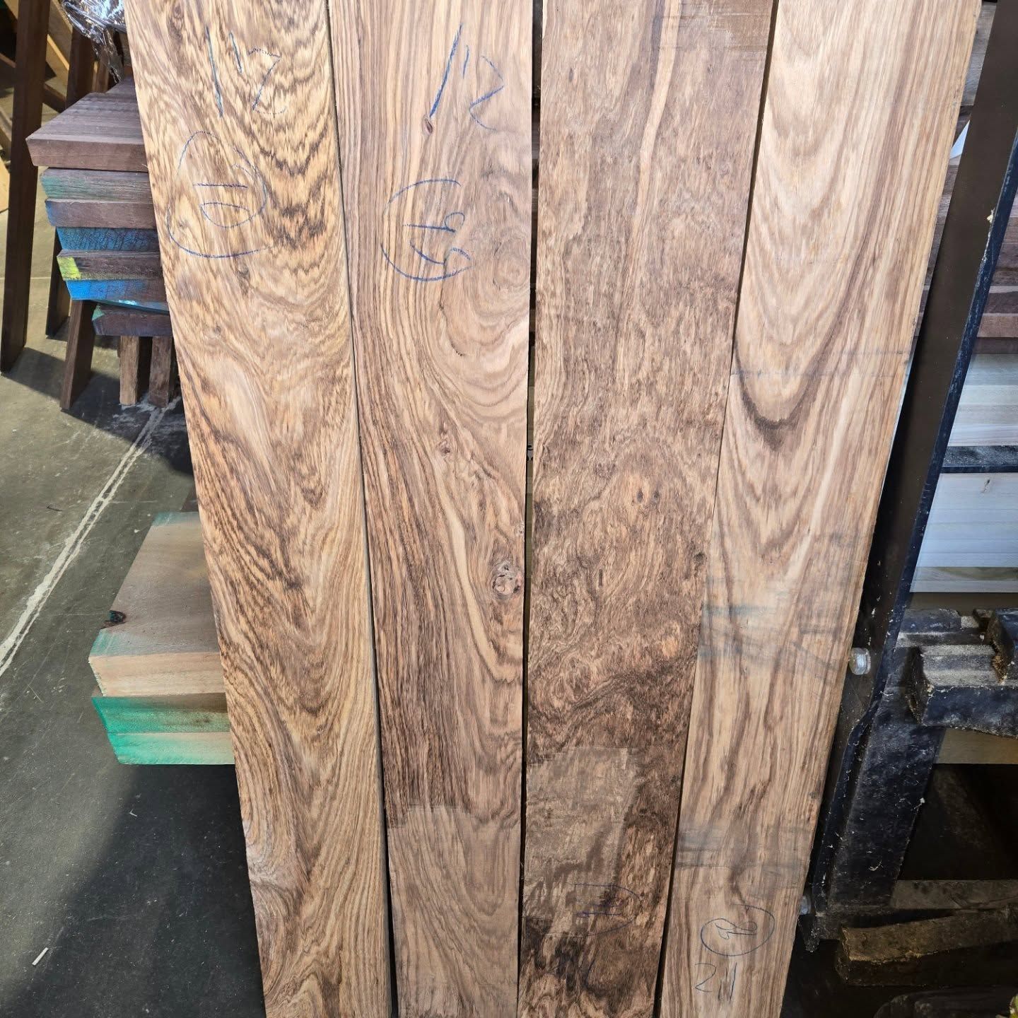 Four vertical wooden boards featuring intricate, swirling grain patterns in shades of brown, displayed in a workshop.
