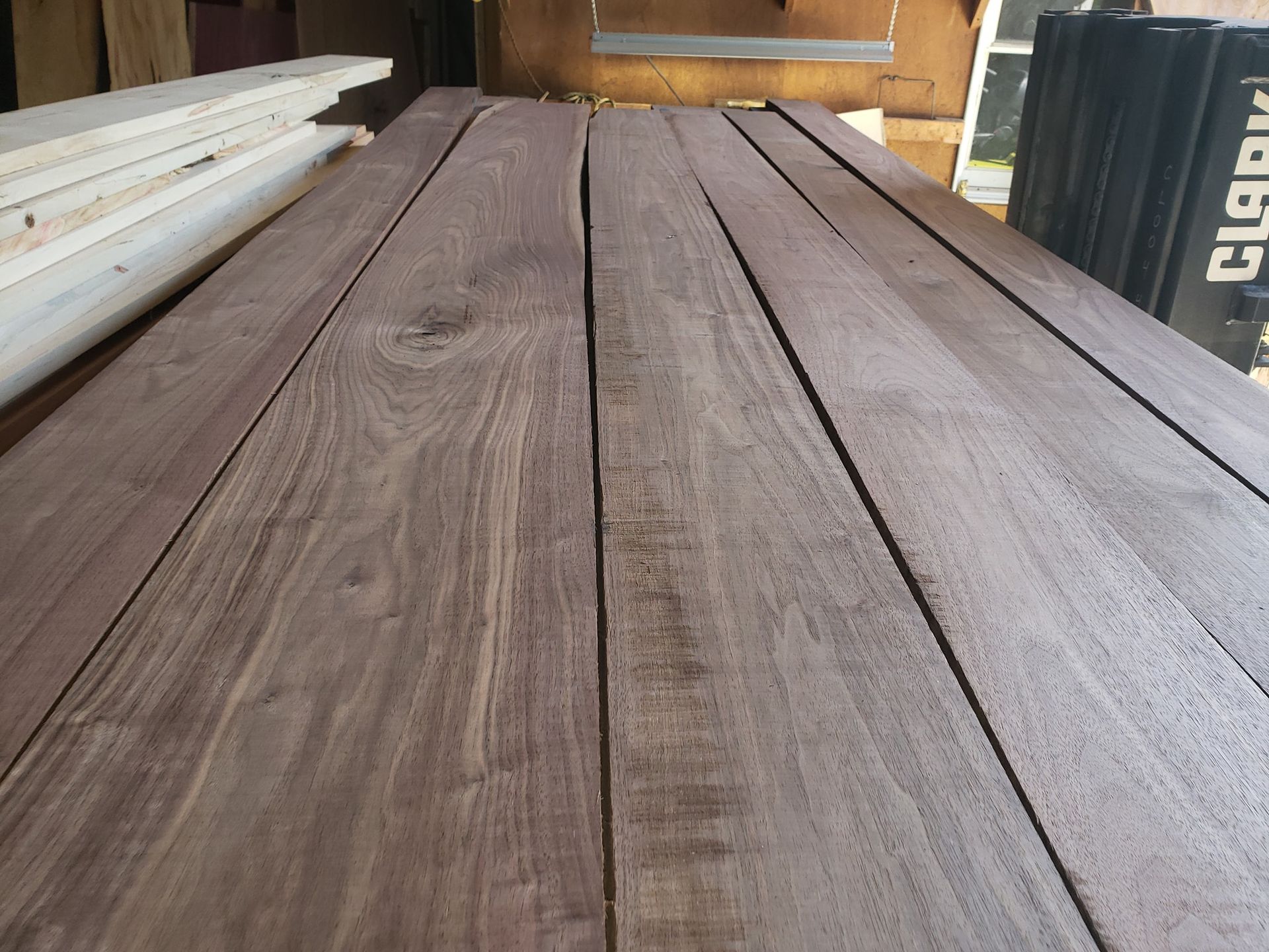 Several rough-cut, dark brown wooden boards are stacked side-by-side in a workshop setting.