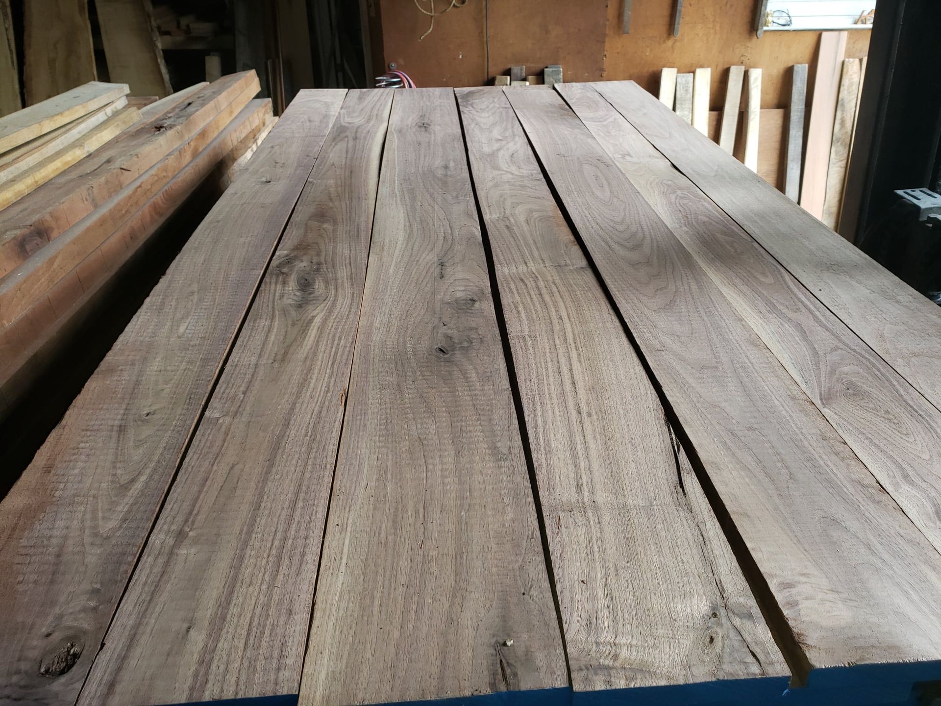 Several boards of raw, brown, unfinished walnut lumber arranged side-by-side in a workshop setting.
