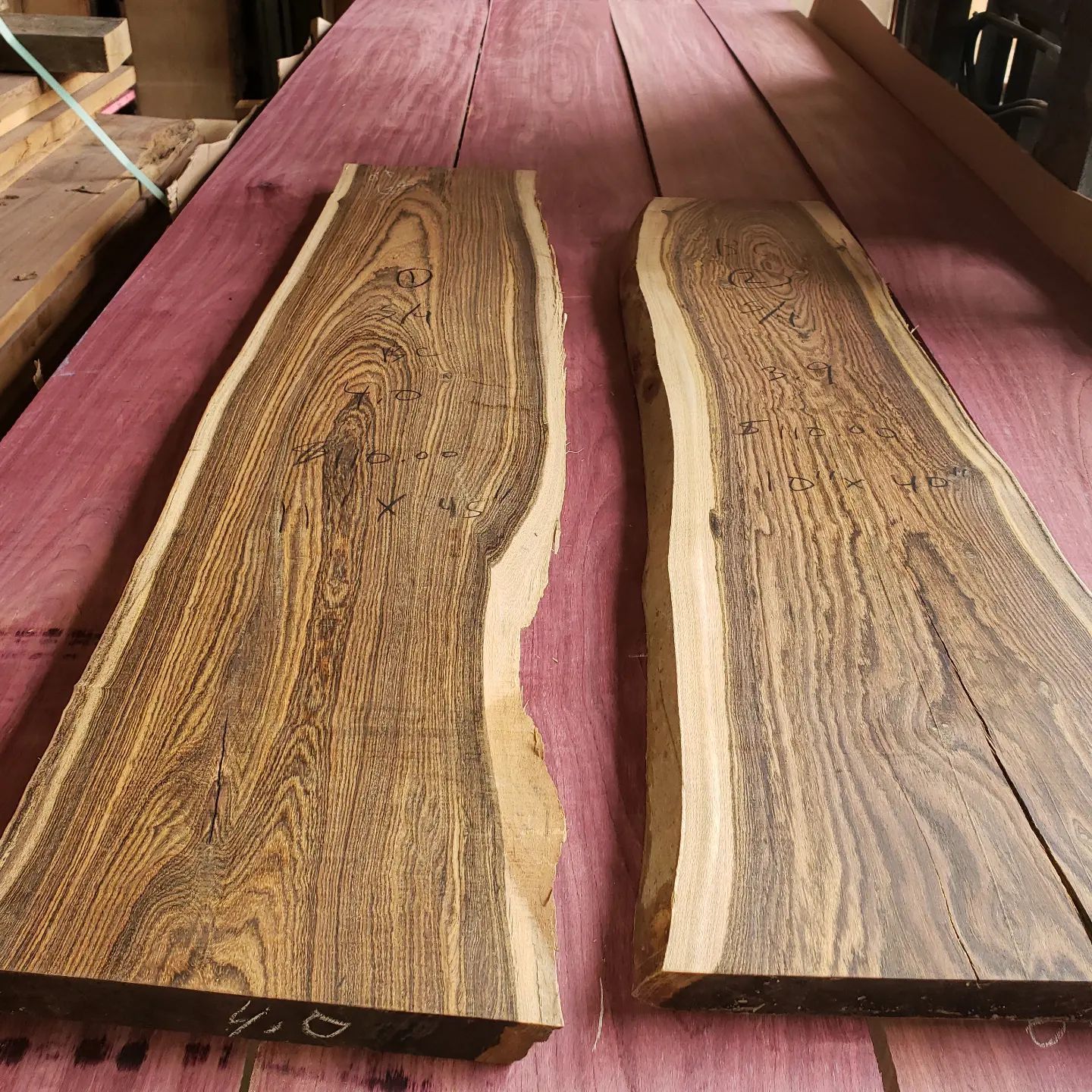 Two live-edge wooden slabs with prominent dark brown and tan wood grain resting on purple-hued lumber.