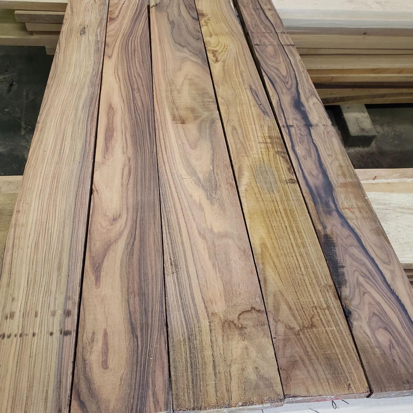 Five rough-cut wooden boards with distinctive dark brown and tan grain patterns arranged side-by-side in a workshop.