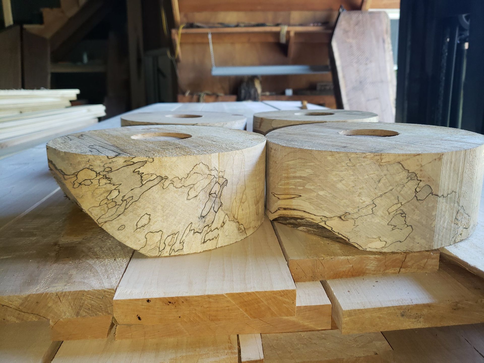Two cylindrical pieces of spalted wood with dark, intricate patterns, resting on wooden boards in a woodworking shop.