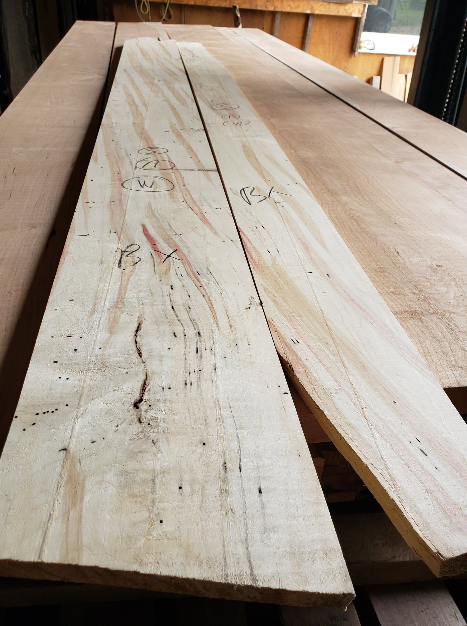Two long, unfinished light-colored wooden planks with natural wood grain and small markings lie on a flat surface.