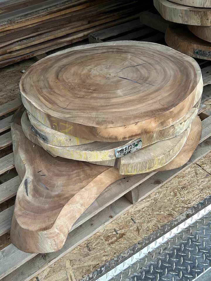 Stacked round wood slices and one irregular slab of raw timber resting on a shipping pallet.