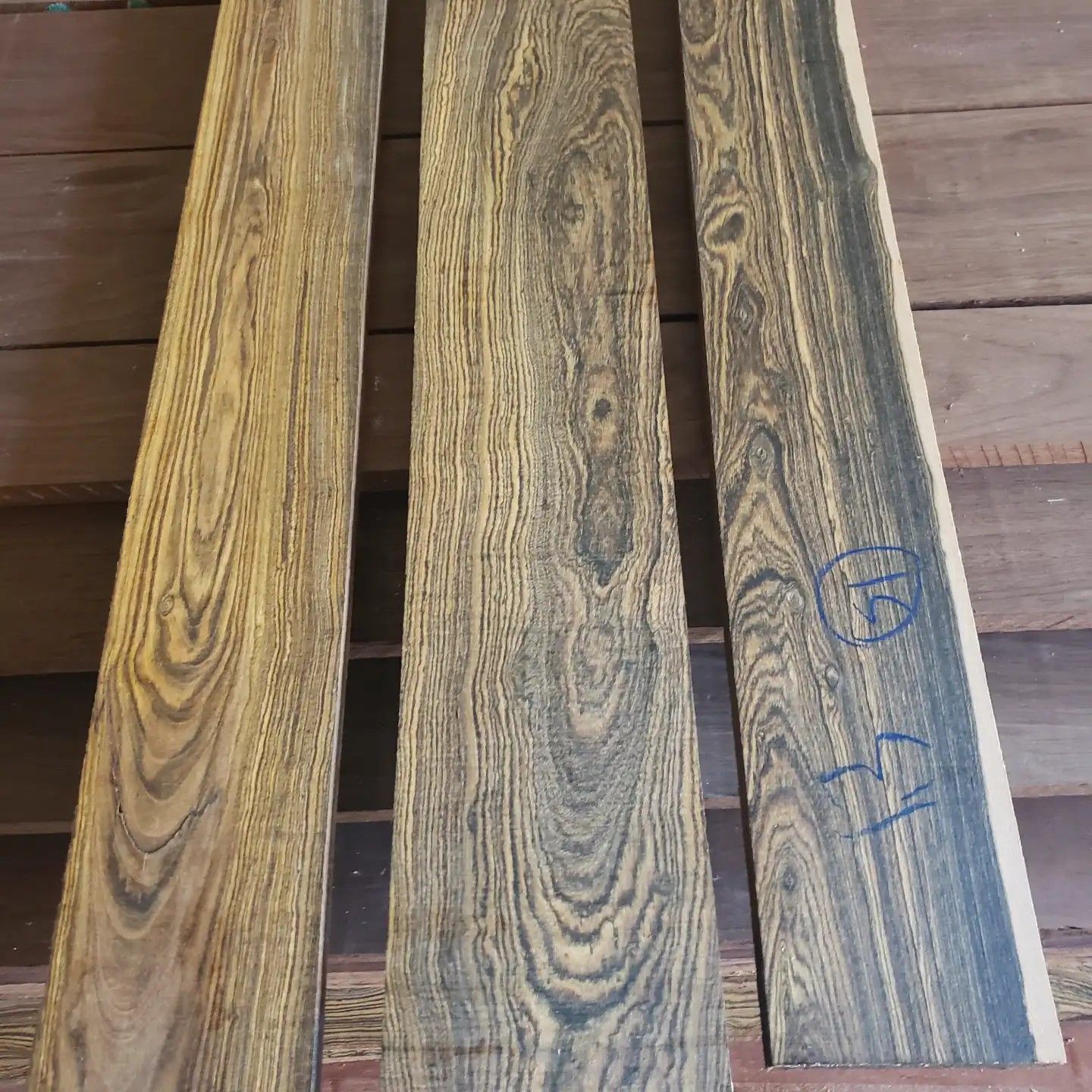 Three long, rectangular planks of dark-streaked, light-brown wood grain sit side-by-side on a wooden surface.