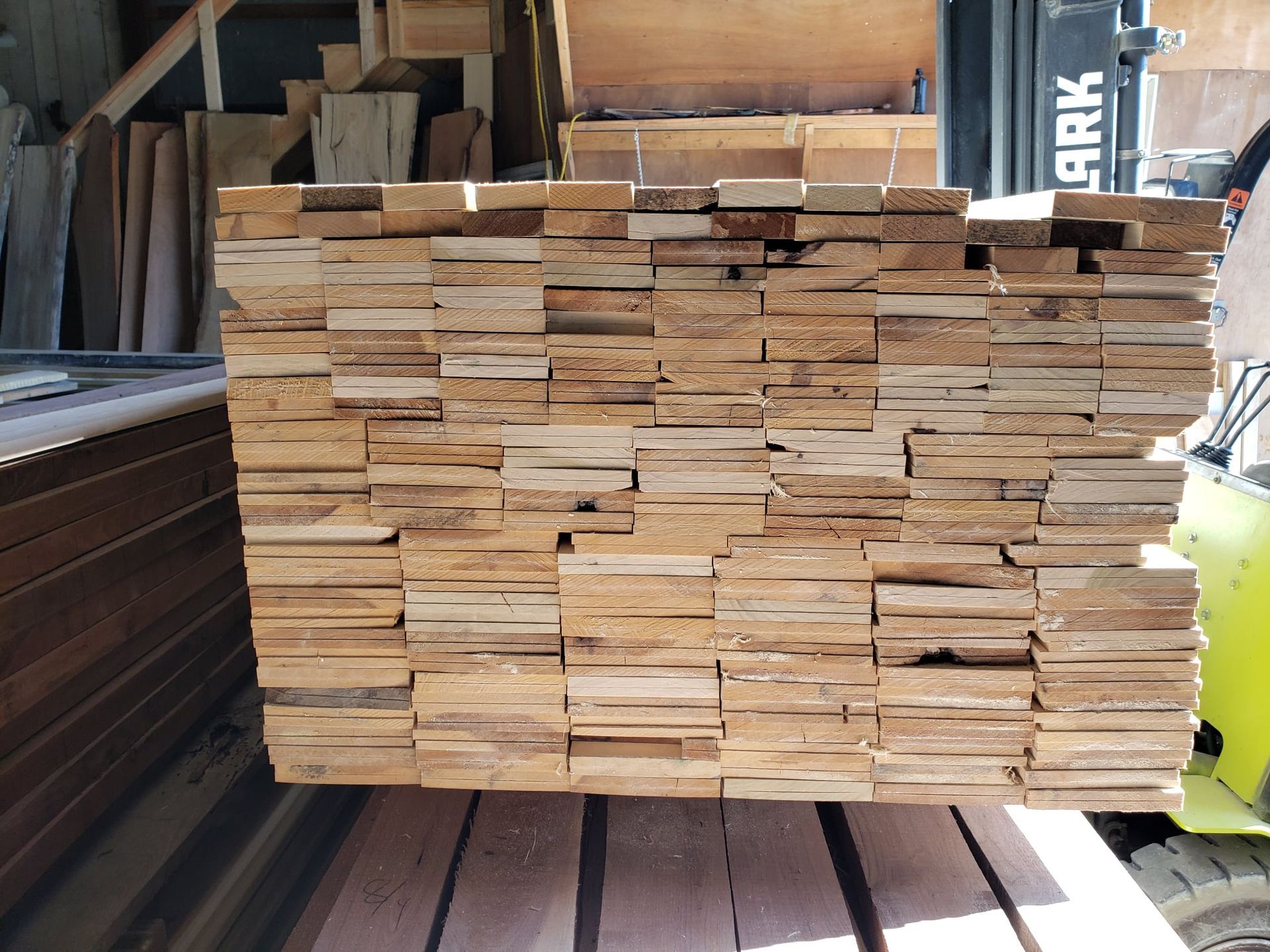 A large, tall stack of light-colored, rectangular wooden planks stored in a warehouse or workshop setting.