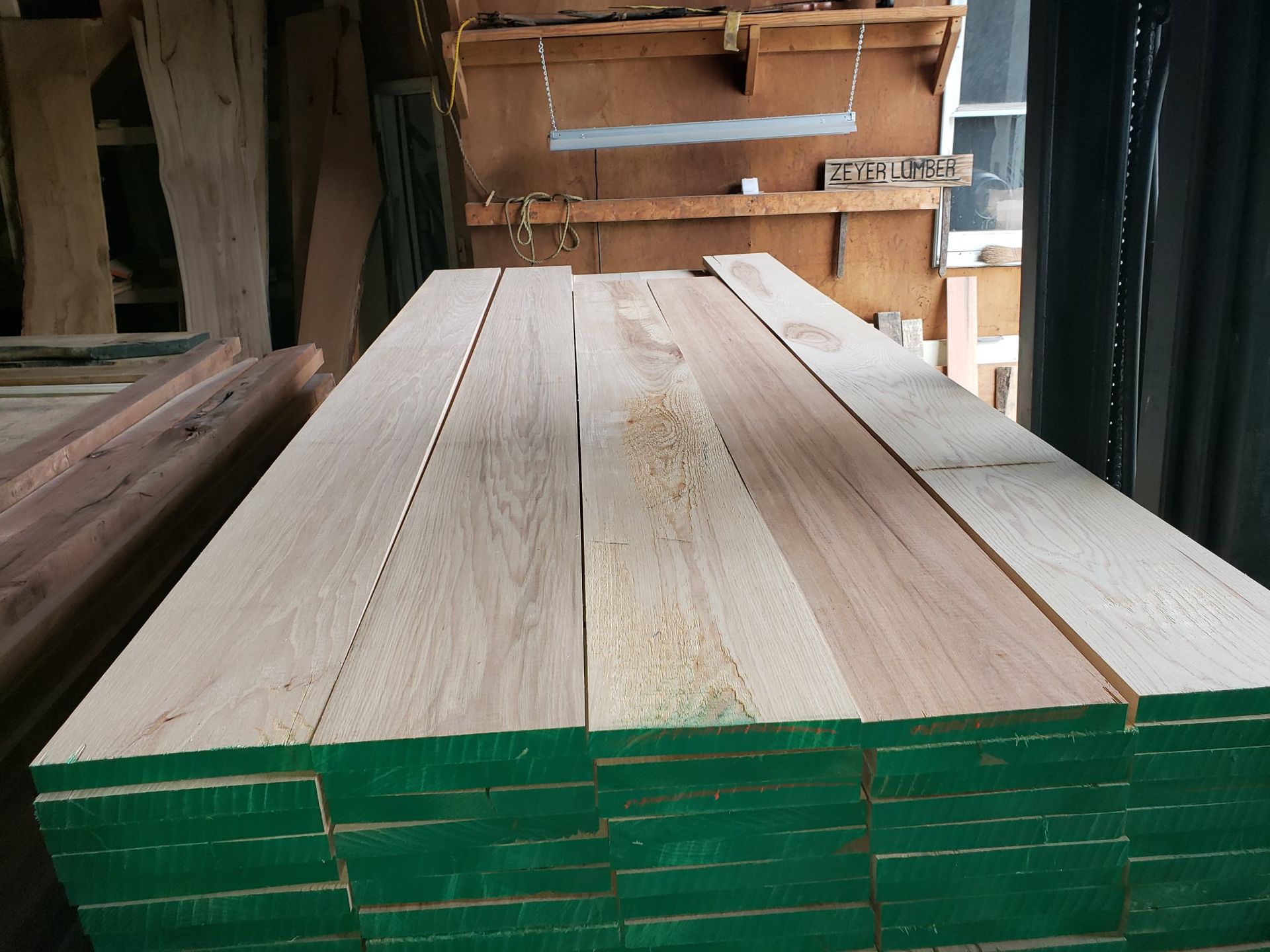 A stack of sawn wooden boards with bright green ends stored in a workshop.