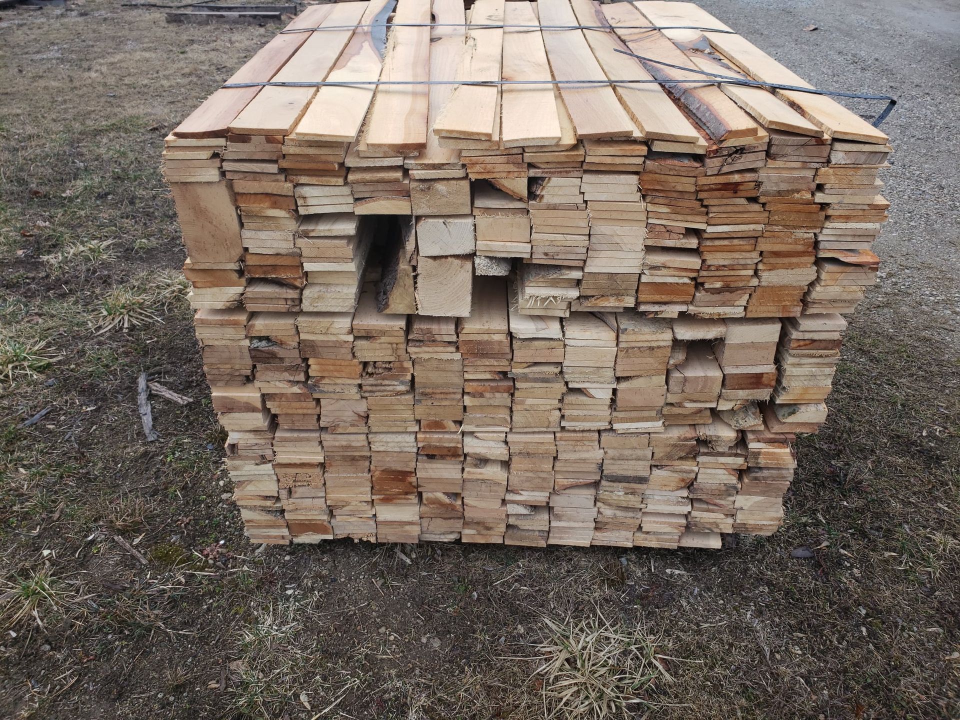 A large, tightly stacked bundle of sawn wooden boards resting on the ground outdoors.