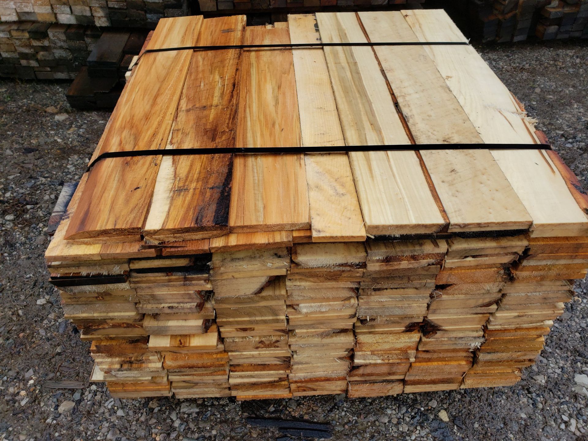A pallet of stacked wooden planks, with a mix of dark, weathered wood on the left and light, raw wood on the right.
