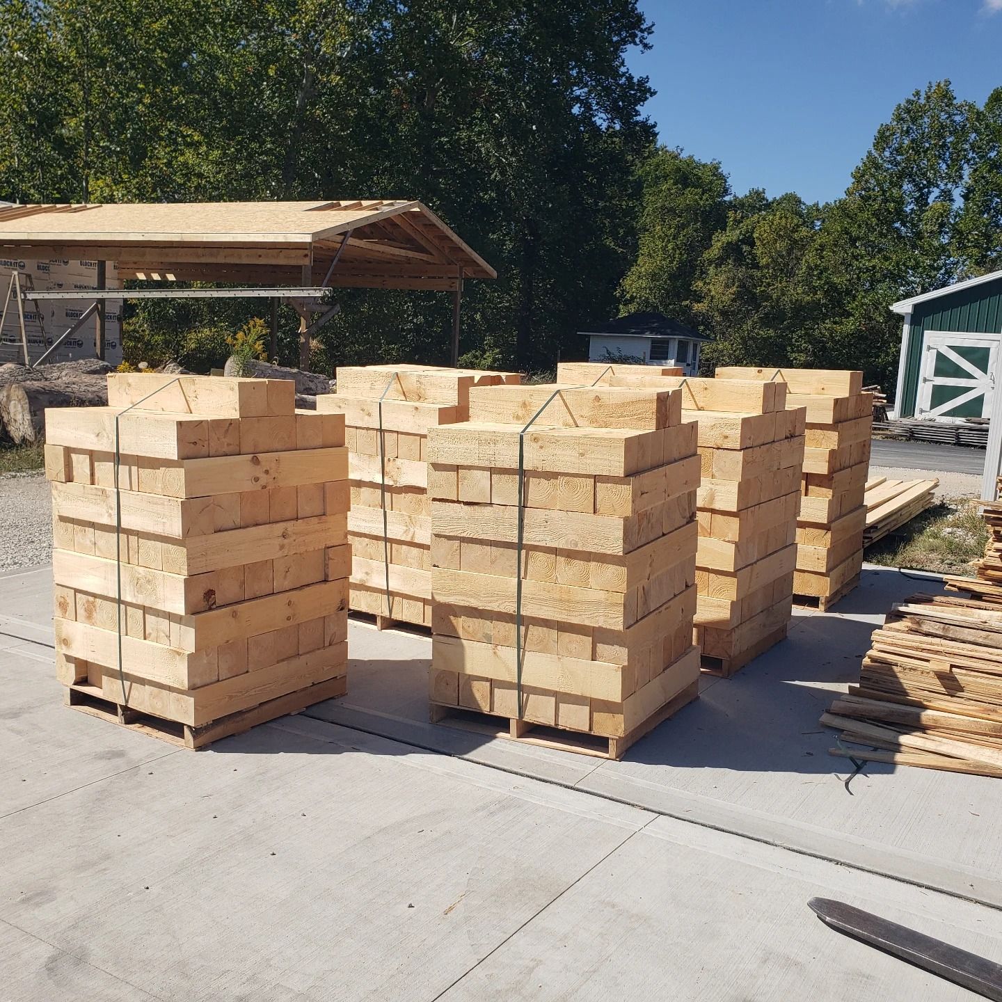 Several stacks of rectangular wooden beams are secured with metal bands on a concrete surface outdoors.