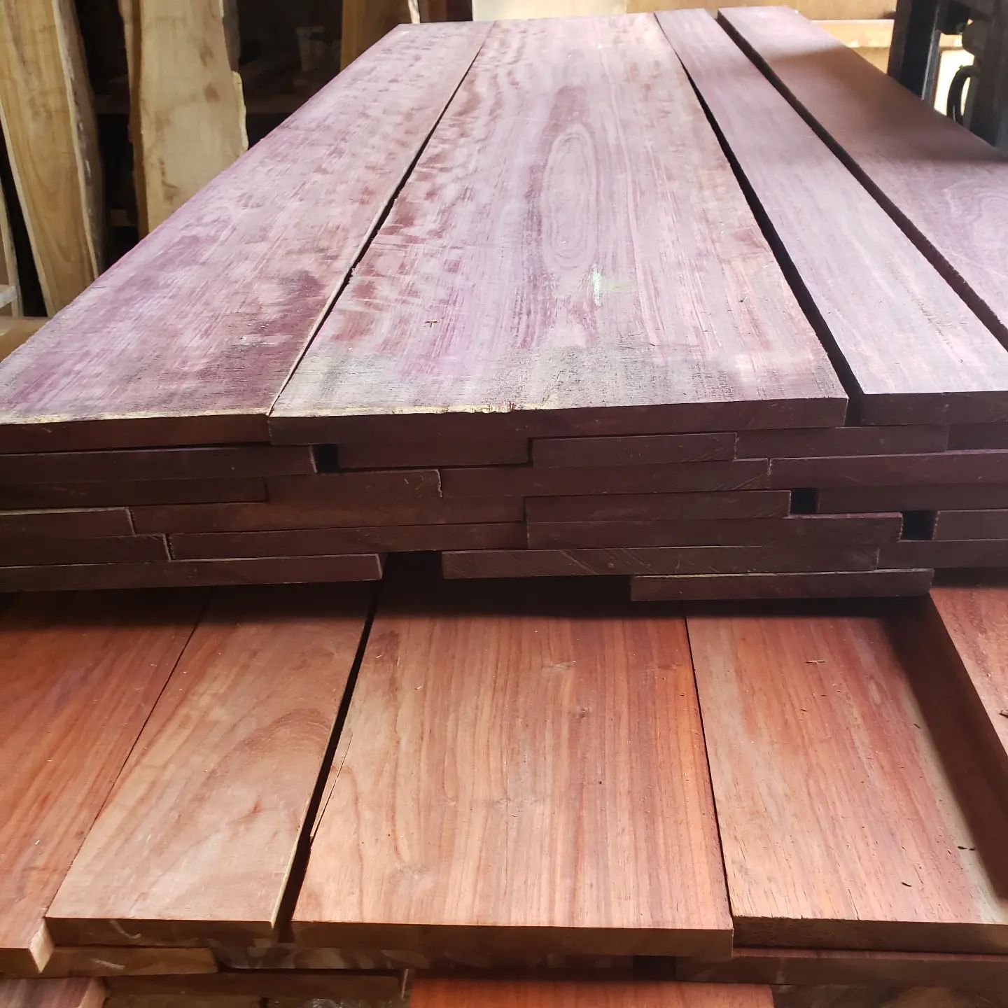 Stacked purple heart and reddish-brown wooden planks in a lumber yard.
