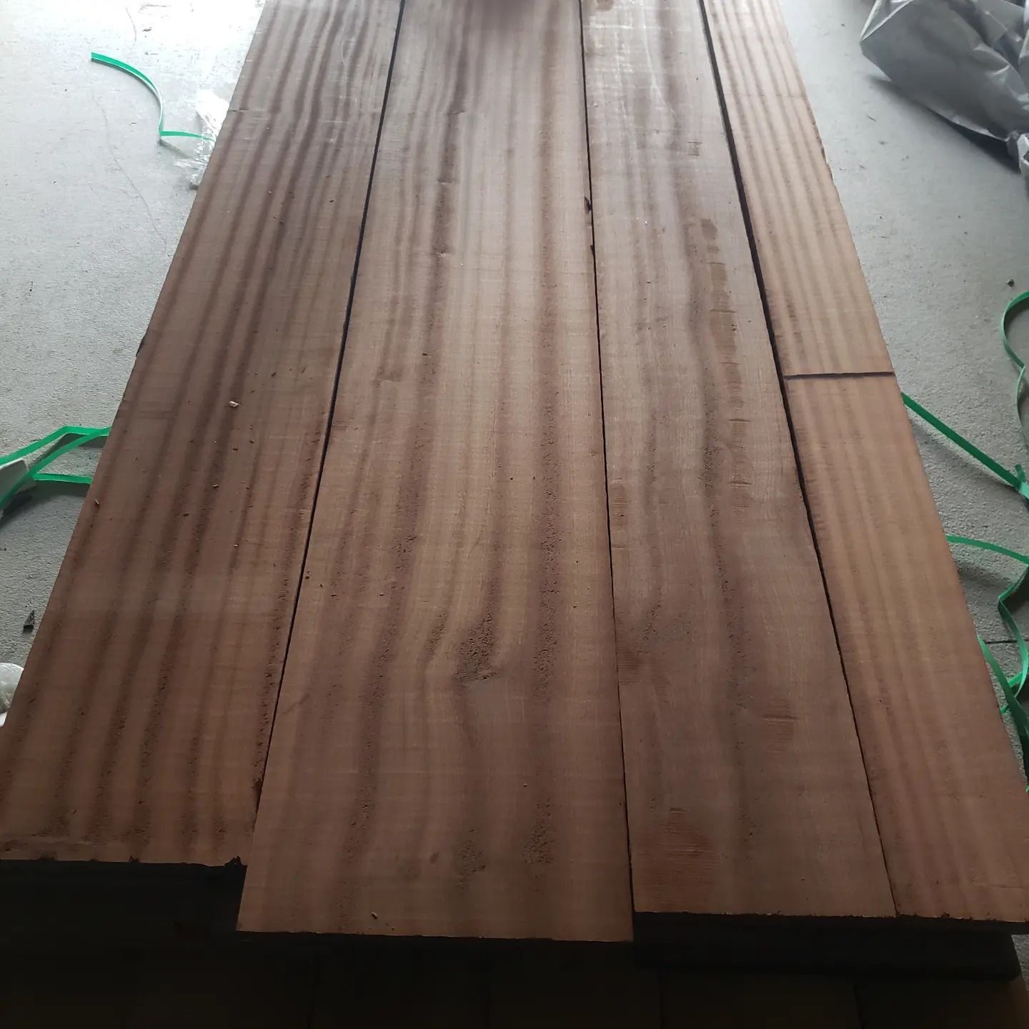 Four parallel, reddish-brown wooden planks with distinct wavy grain patterns laid side by side on a concrete surface.
