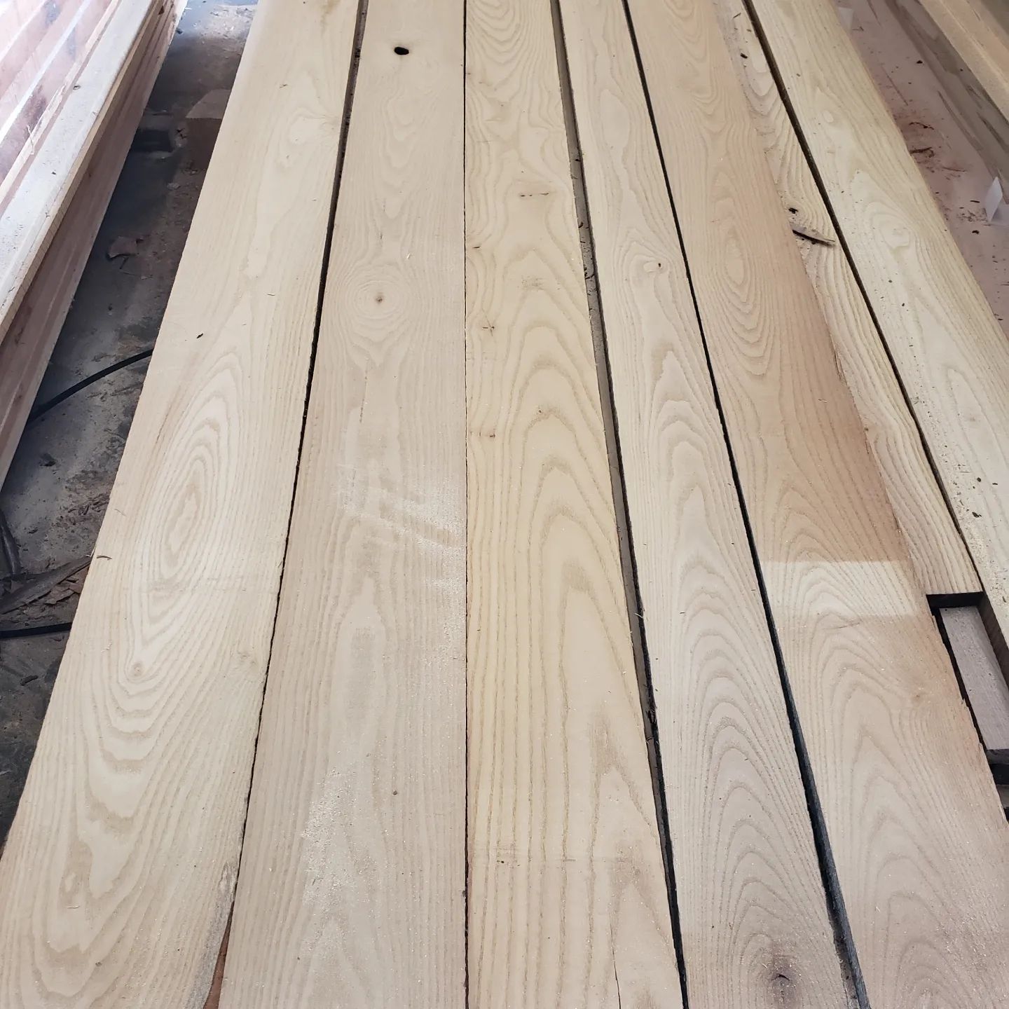 Several long, light-colored wooden planks laid side-by-side in a workshop setting.