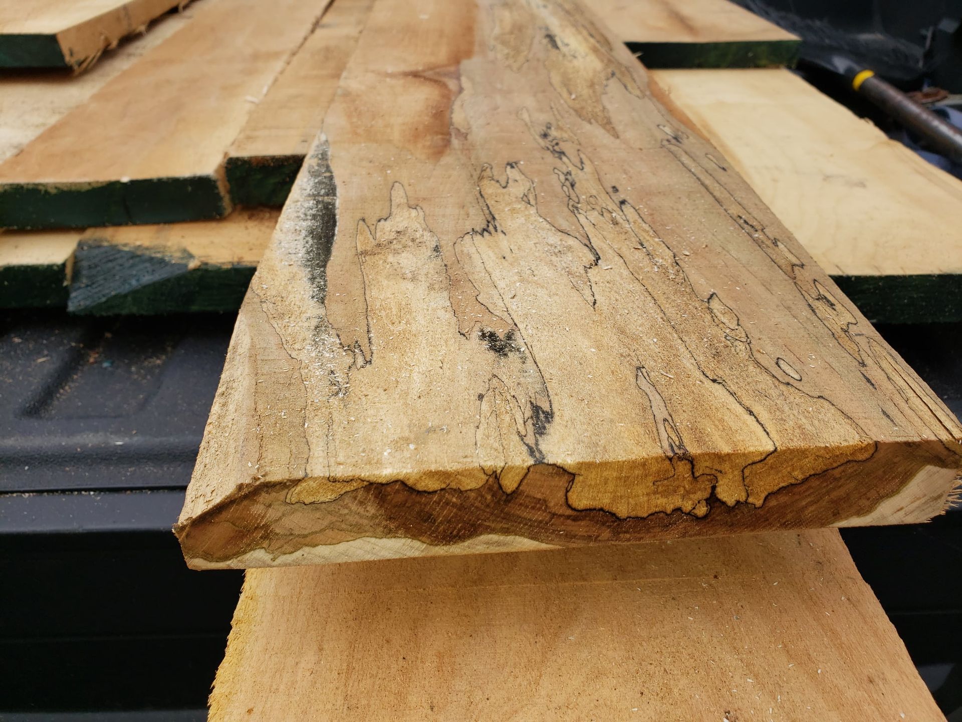 Spalted wood board showing distinct dark fungal lines and color variation, sitting atop a stack of lumber in a truck bed.