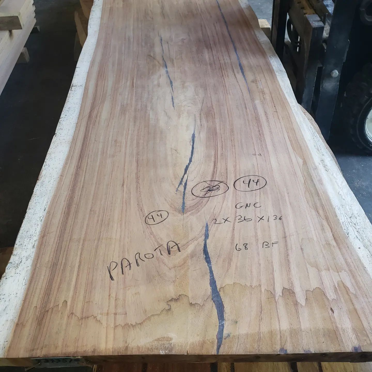 A large Parota wood slab with prominent natural cracks, resting on supports in a warehouse setting.